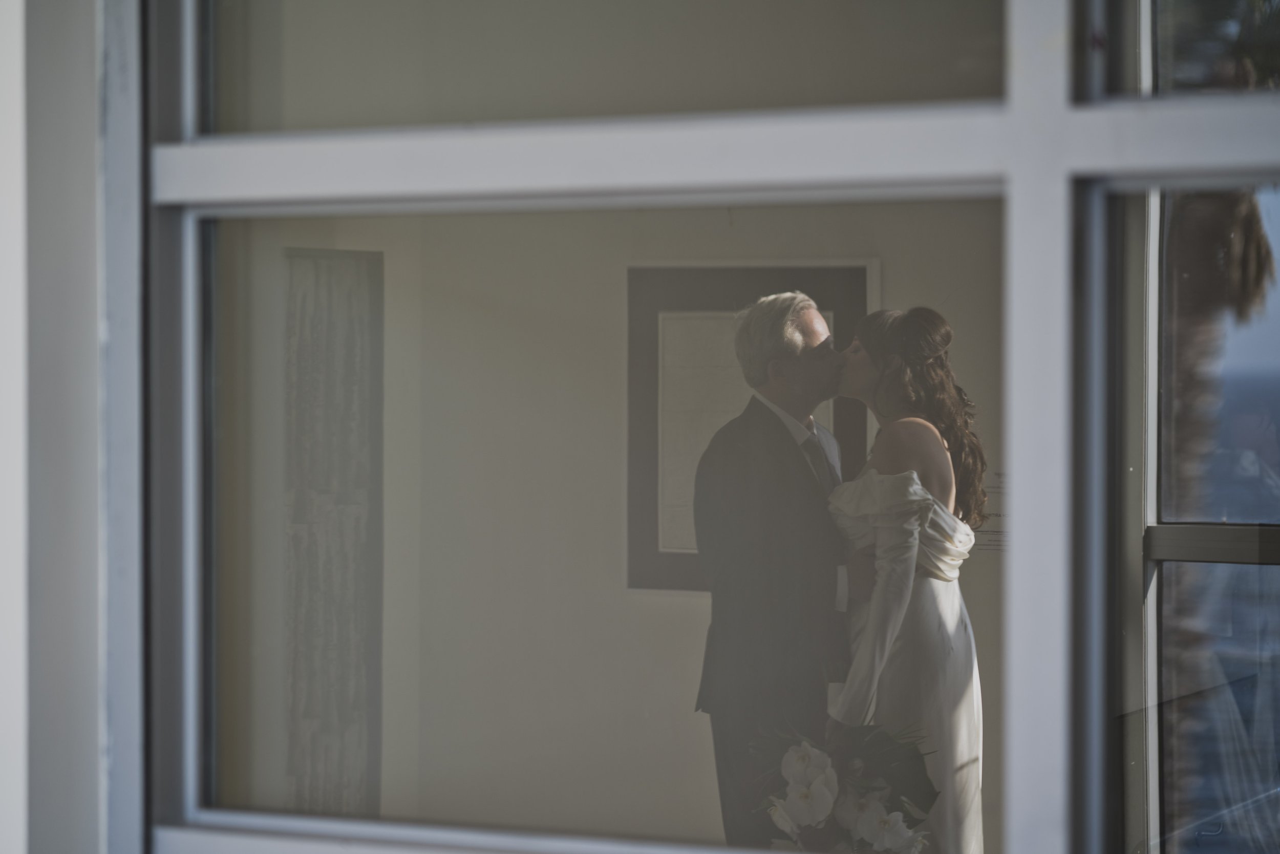 Bride and groom sharing a quiet kiss reflected through a window during their destination wedding portraits.