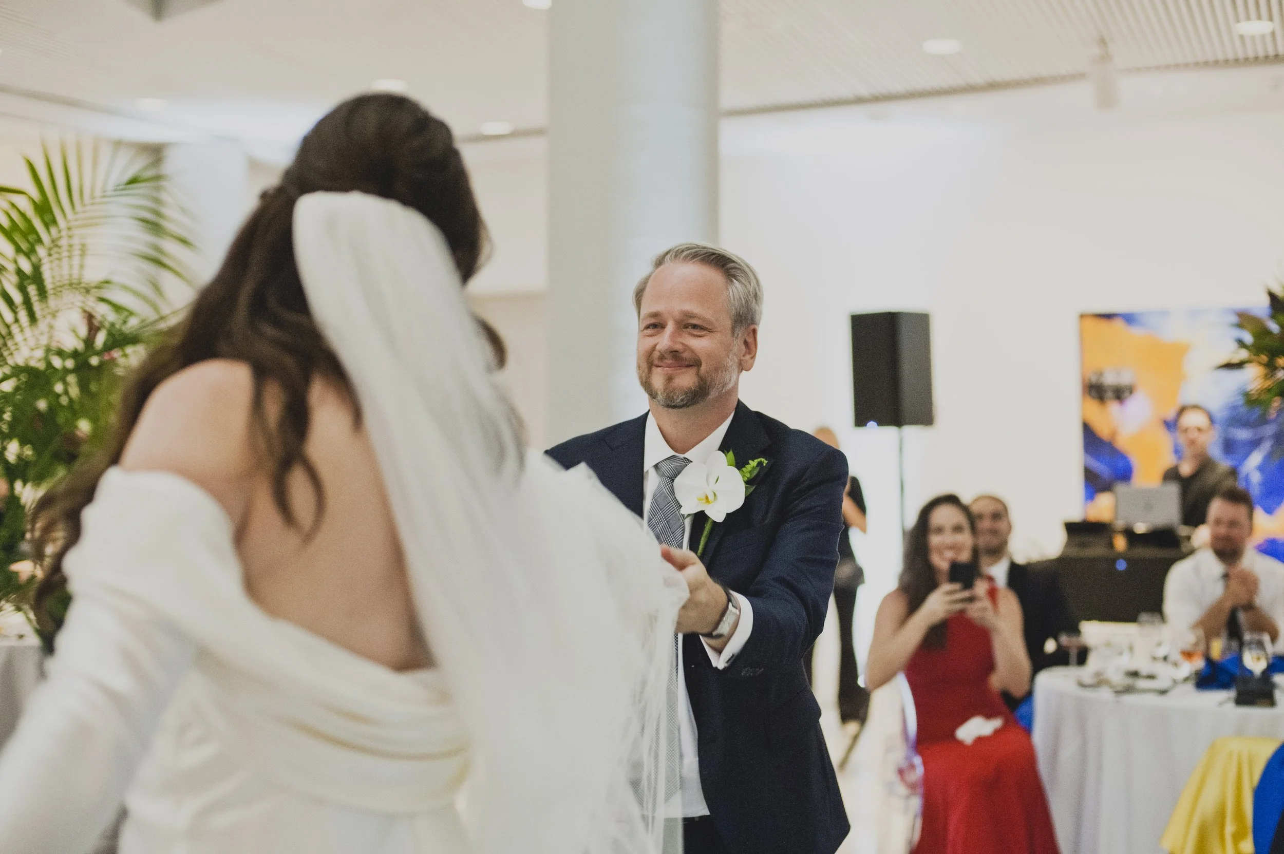 Groom smiling as he dances with his bride during their first dance while wedding guests watch and celebrate at a modern reception.