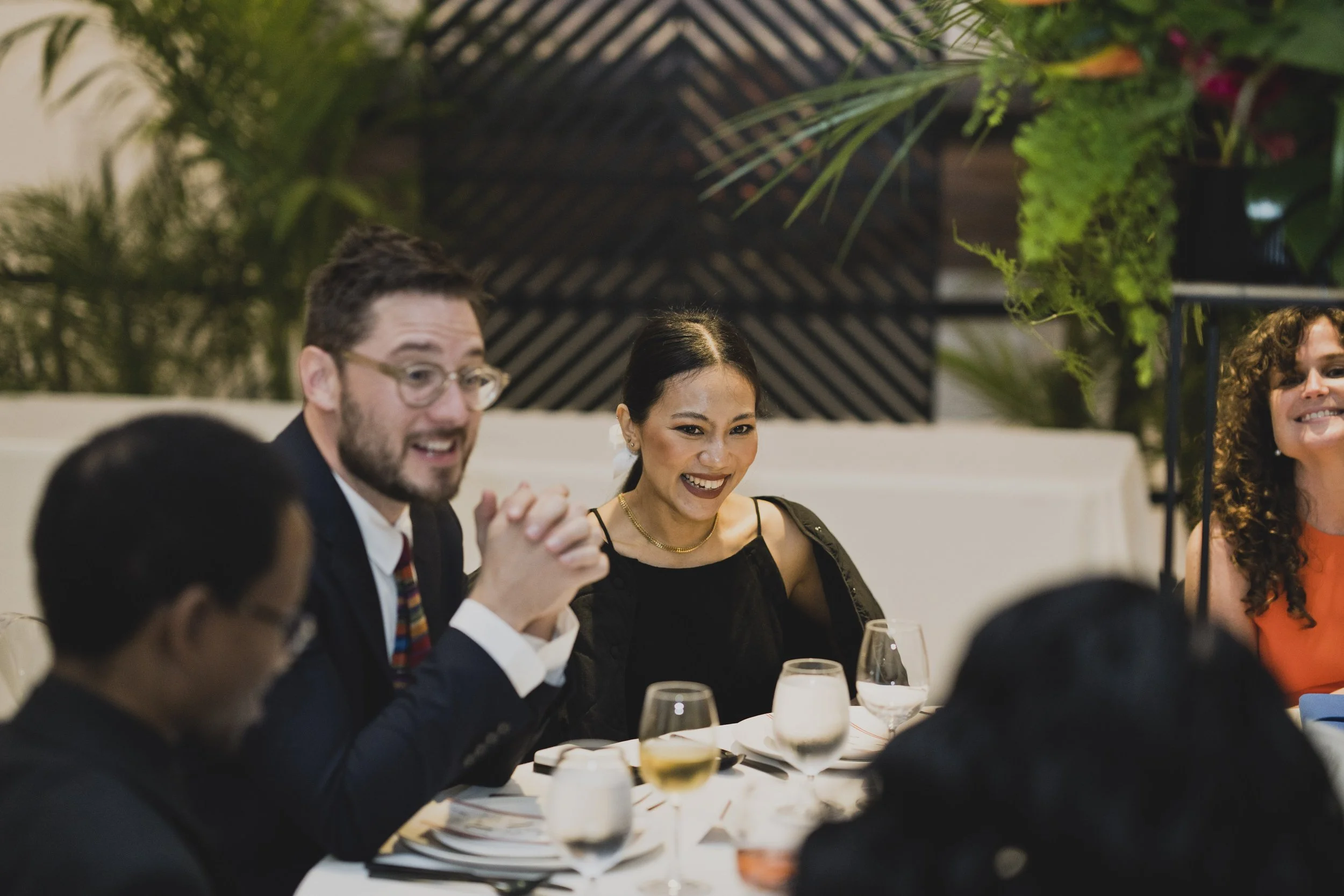Wedding guests smiling and enjoying dinner together during a contemporary museum wedding reception with tropical floral centerpieces.