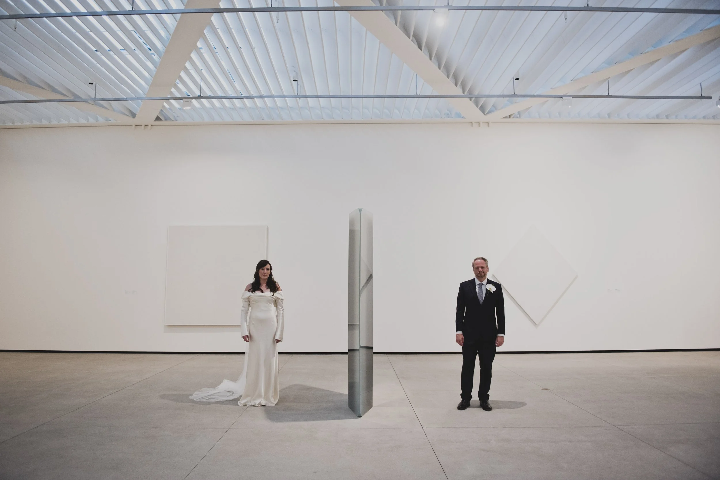 Bride and groom standing apart in a spacious contemporary art gallery, framed by minimalist architecture and geometric modern art.