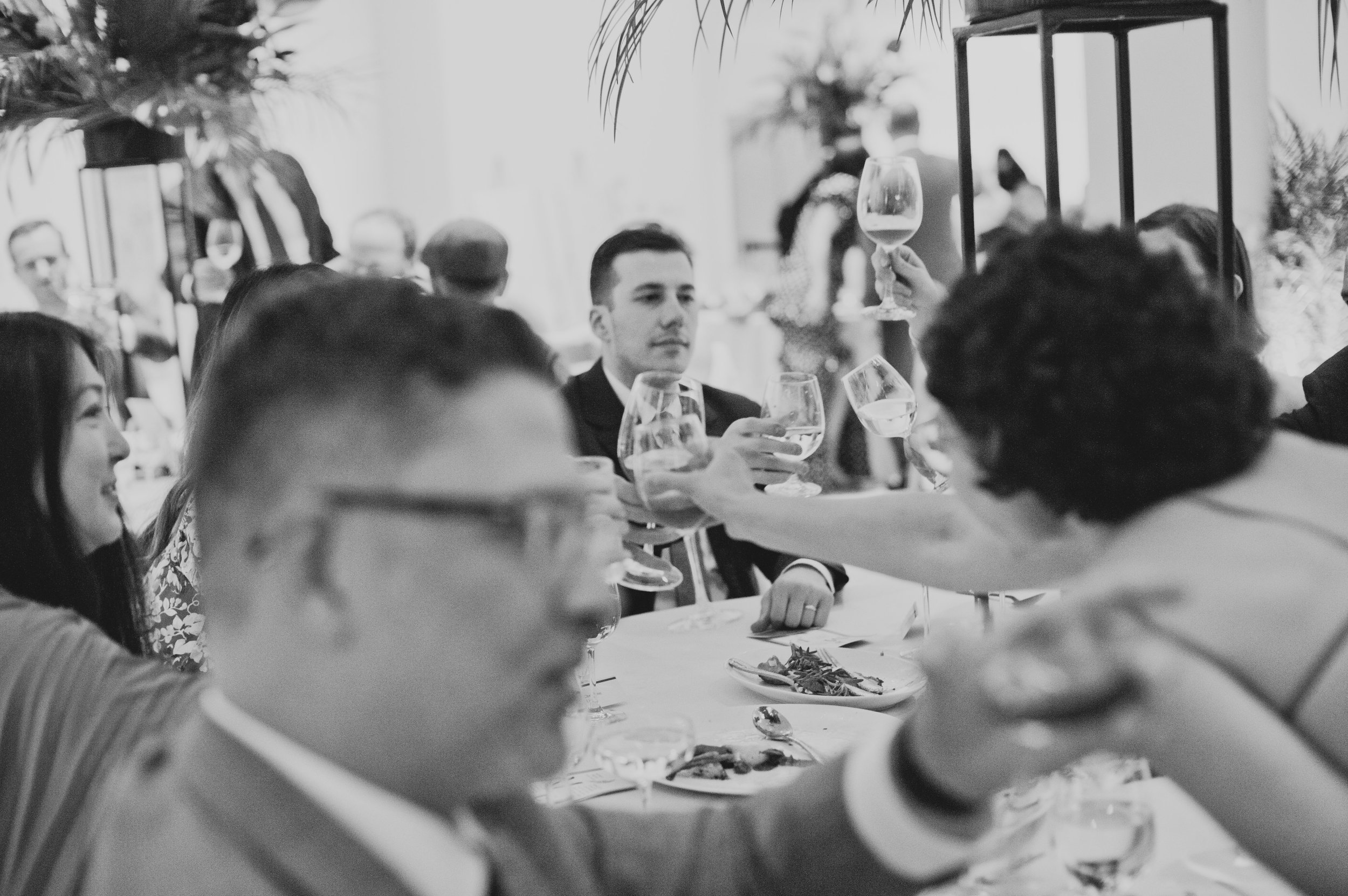 Wedding guests raising their glasses together in a celebratory toast during a modern museum wedding reception.