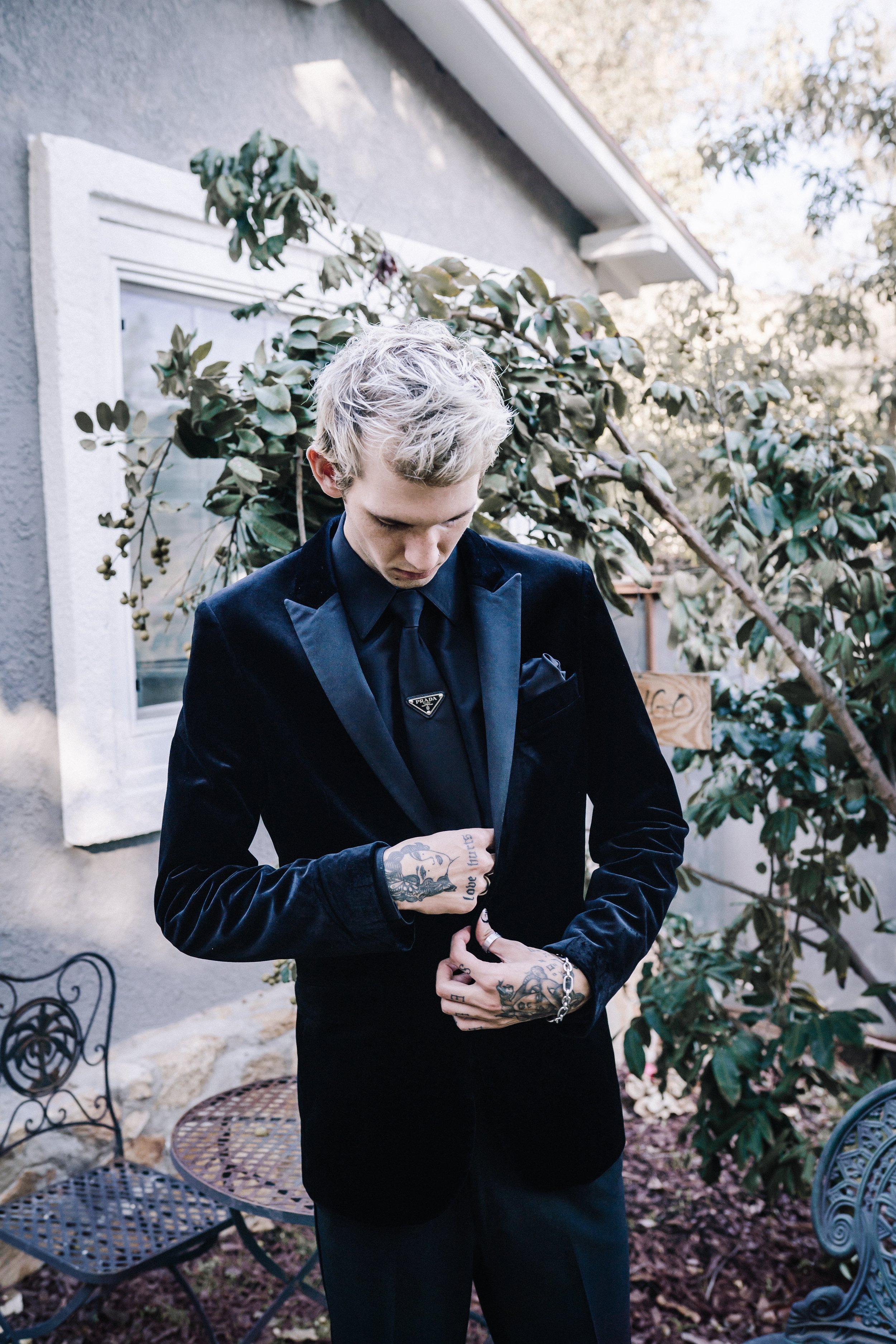 Groom buttoning a black velvet wedding jacket with satin lapels and a Prada tie pin before an alternative wedding ceremony.