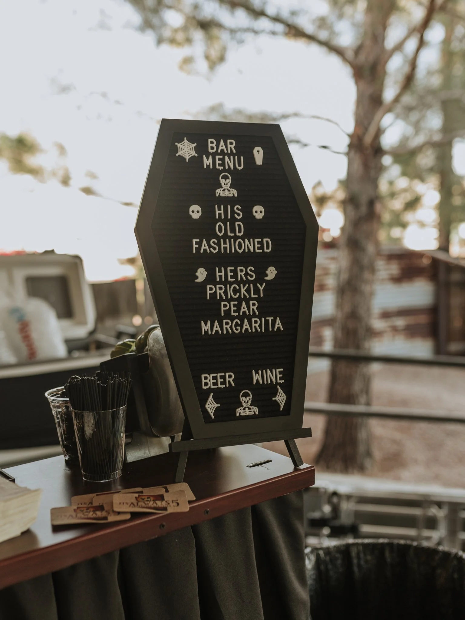Halloween-themed wedding bar menu displayed on a coffin-shaped sign featuring custom signature cocktails, beer, and wine.