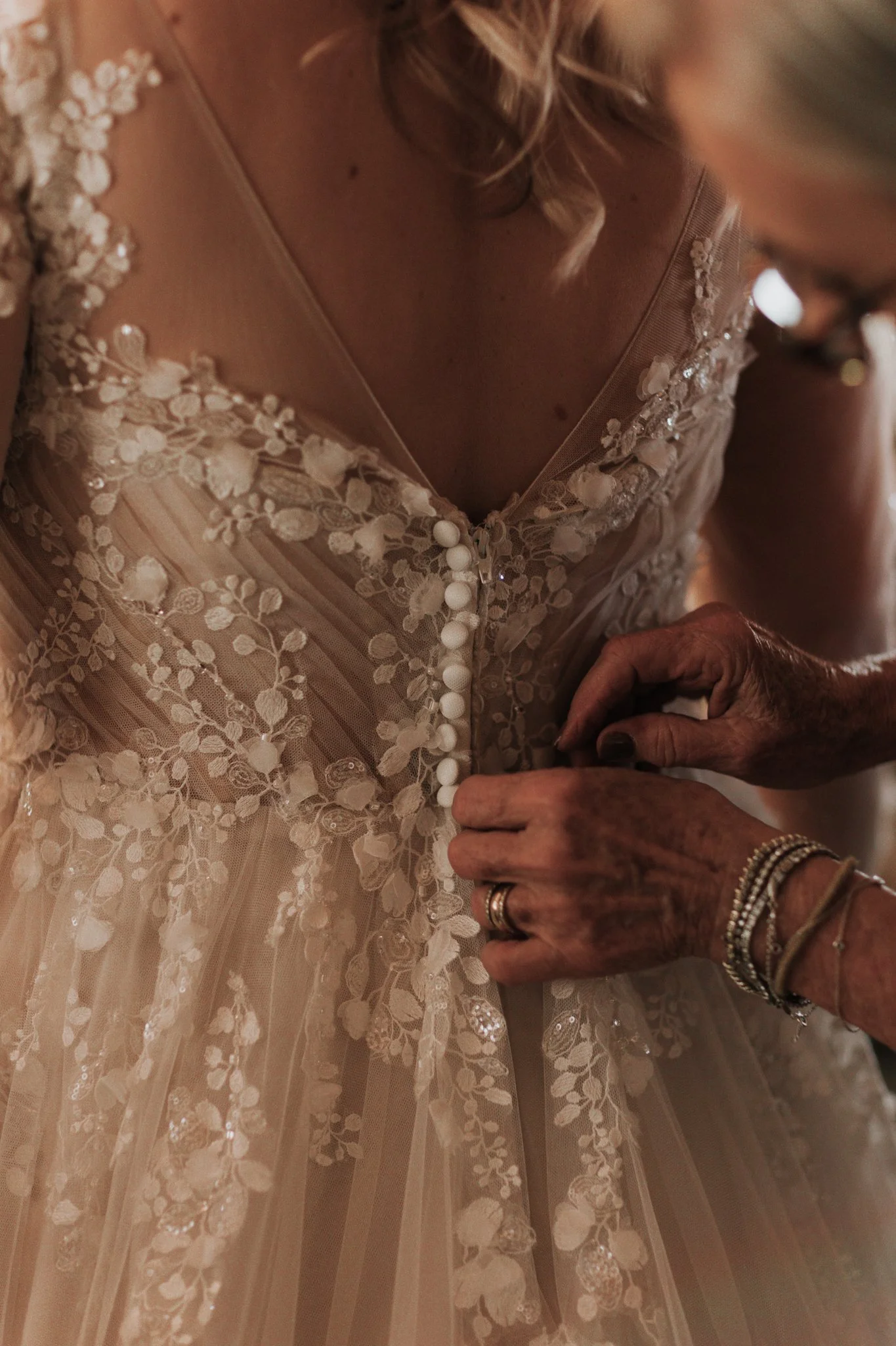 Close-up of hands fastening the delicate buttons on the back of the bride's lace wedding dress while she gets ready.