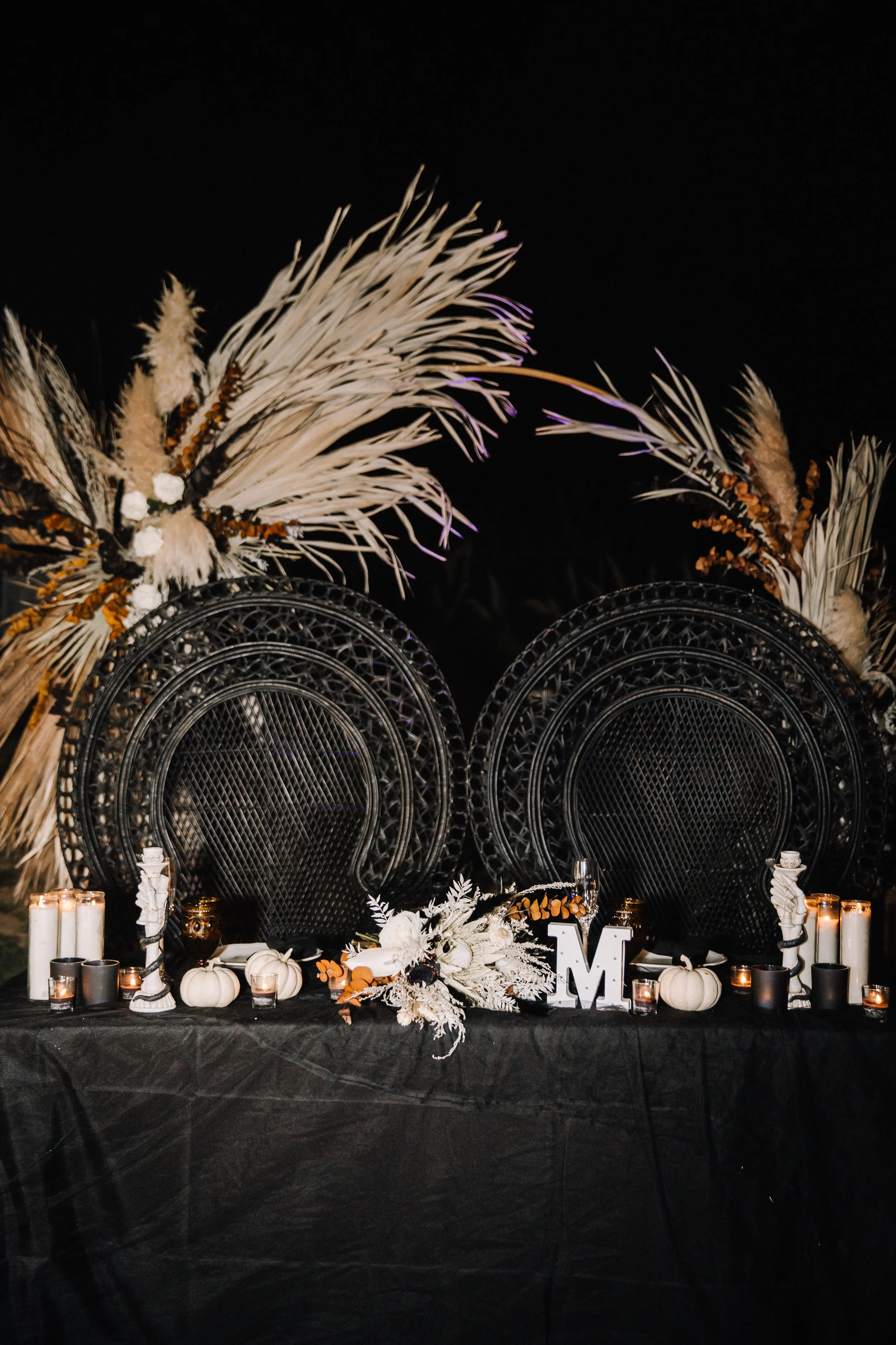 Sweetheart table with black peacock chairs, white pumpkins, candlelight, and dramatic floral arrangements for a dark romantic Halloween wedding theme.