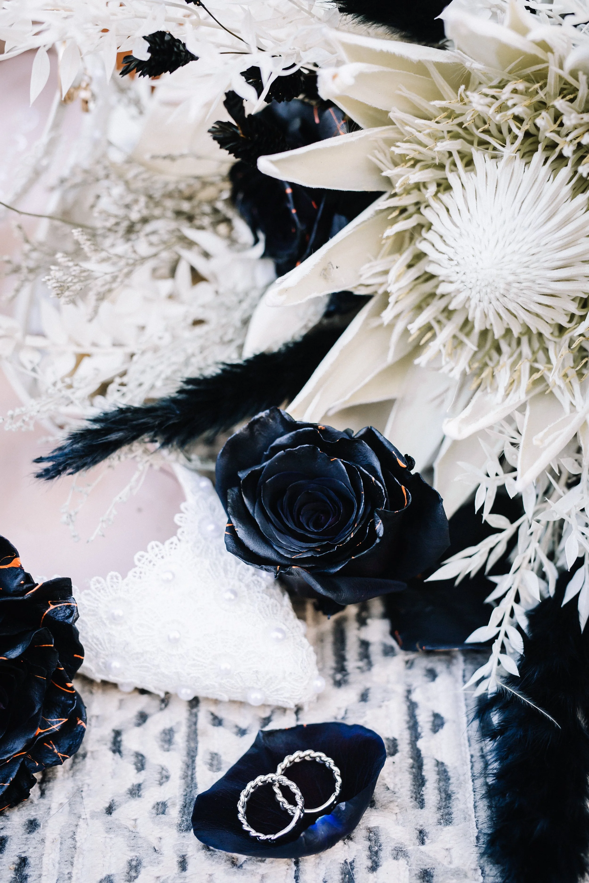 Halloween wedding detail flat lay featuring lace bridal heels, black roses, a coffin ring box, skeleton ring holder, black ribbon, and wedding accessories.