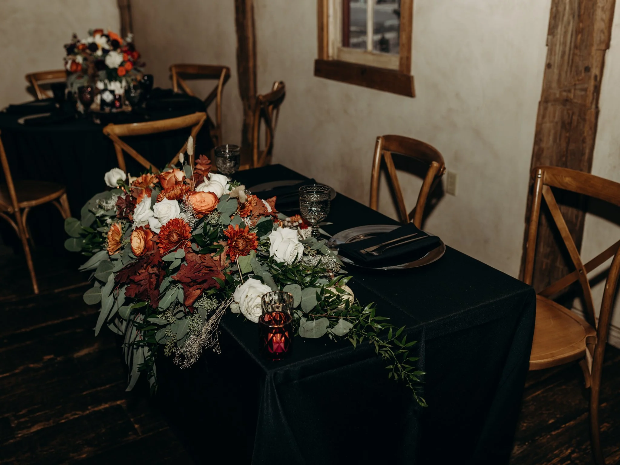 Reception space featuring black table linens, dark place settings, and rich fall floral centerpieces for a modern Halloween wedding.
