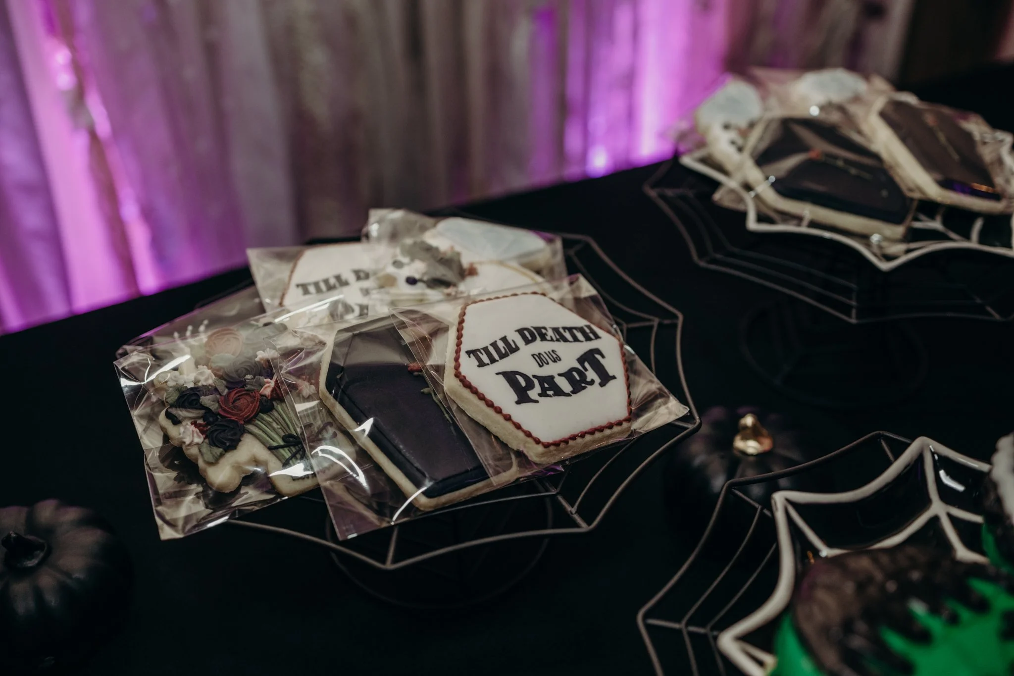 Halloween wedding cookie favors featuring coffin, engagement ring, floral, and "Till Death Do Us Part" designs displayed on black spiderweb serving trays.
