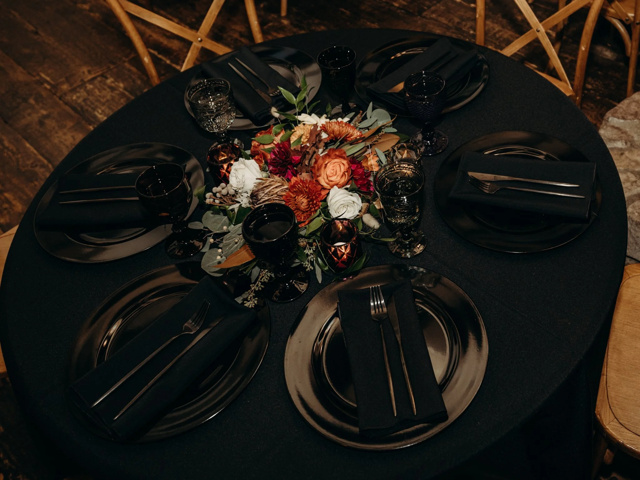 Black dinnerware, dark glassware, black linens, and an autumn floral centerpiece create an elegant Halloween wedding reception tablescape.