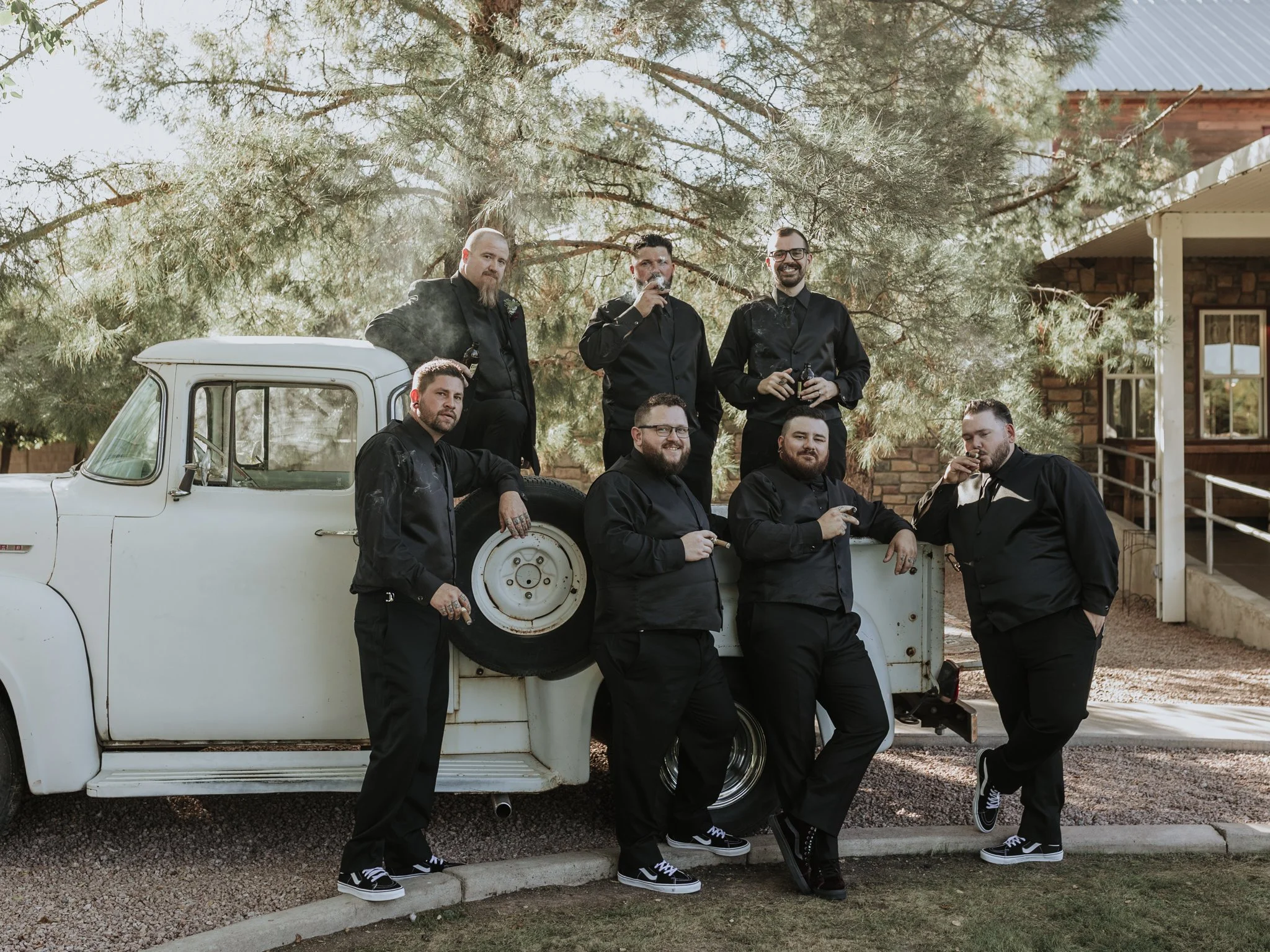 Groomsmen in all-black with cigars beside a vintage truck at a Shenandoah Mill wedding