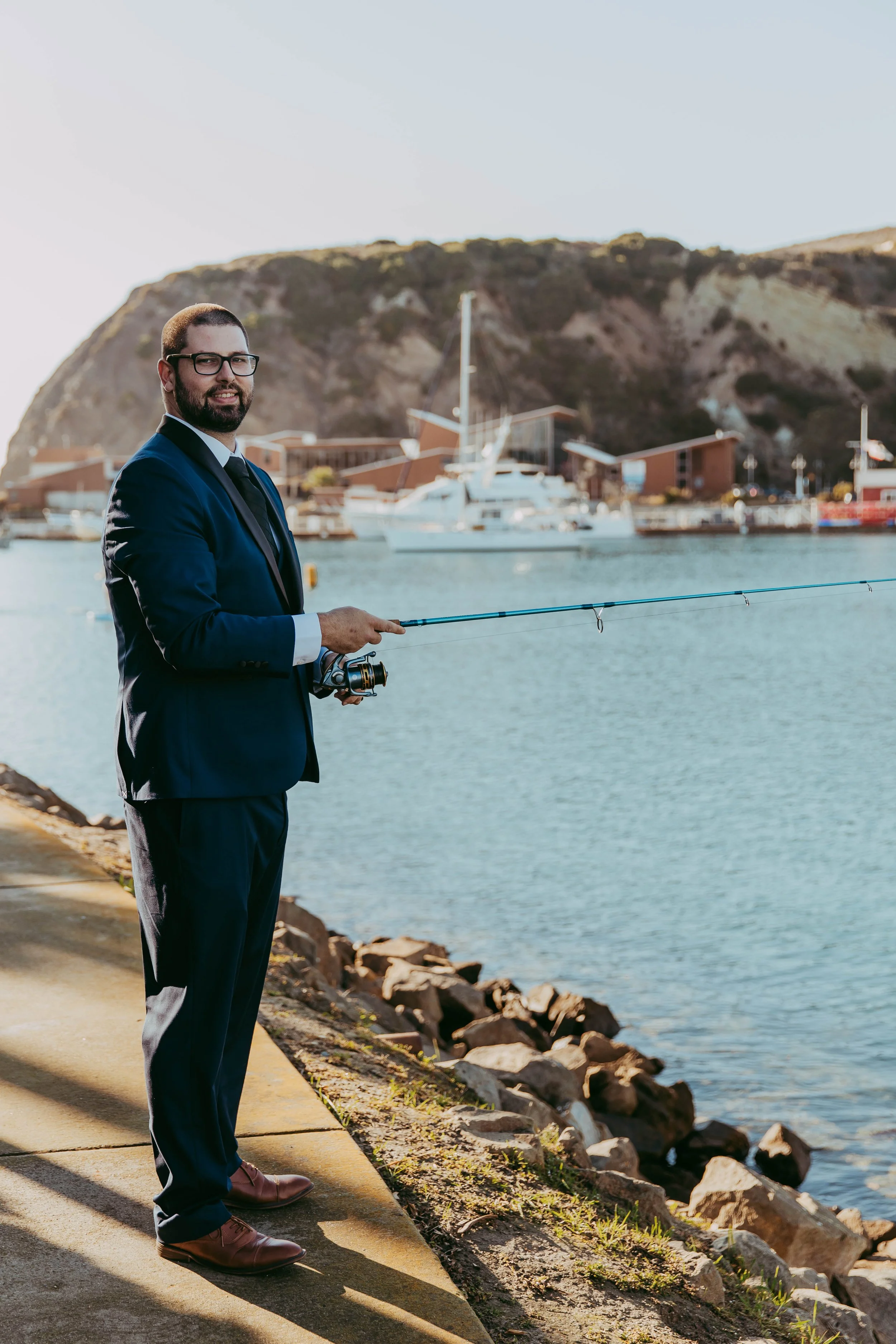 Groom casts a fishing line in his suit along Dana Point Harbor before the ceremony