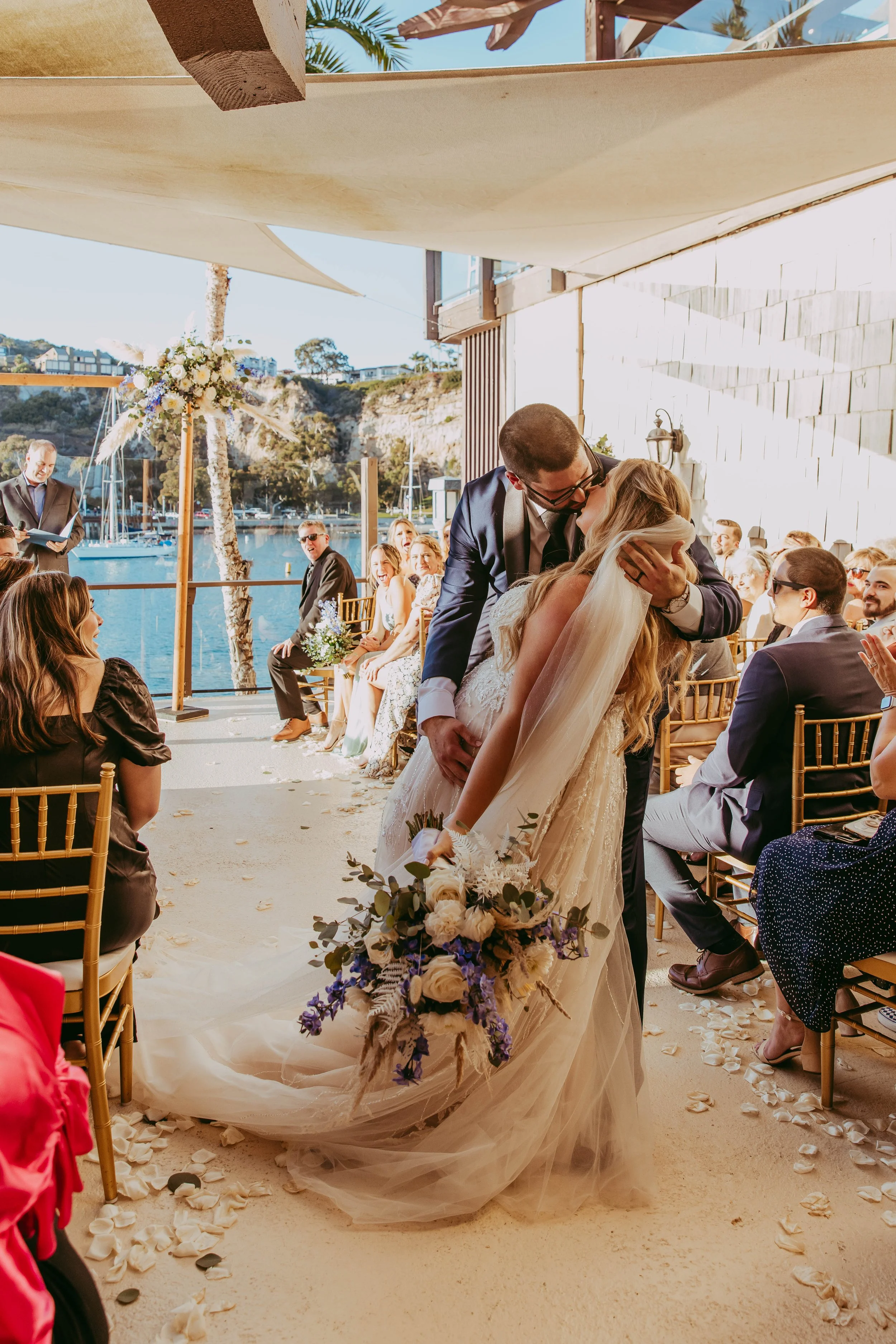 Groom dips the bride for a first kiss at a waterfront Dana Point Yacht Club ceremony
