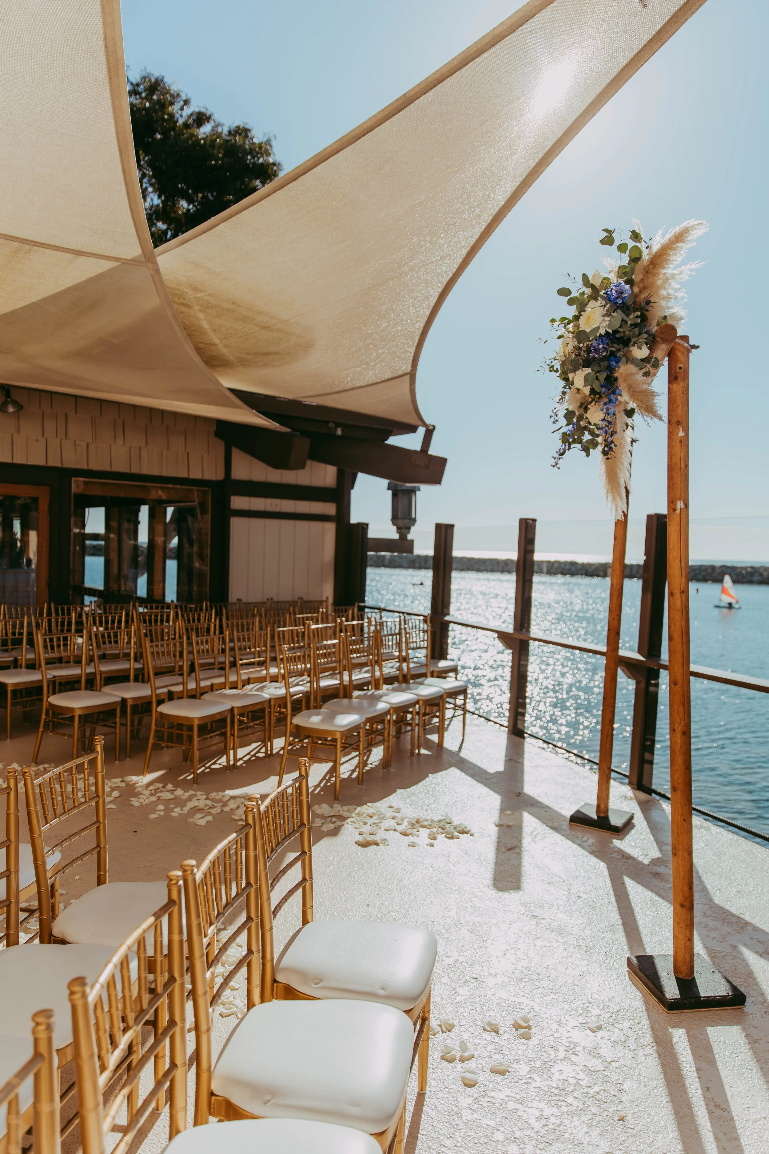 Waterfront ceremony setup with gold chairs and sail shades at Dana Point Yacht Club