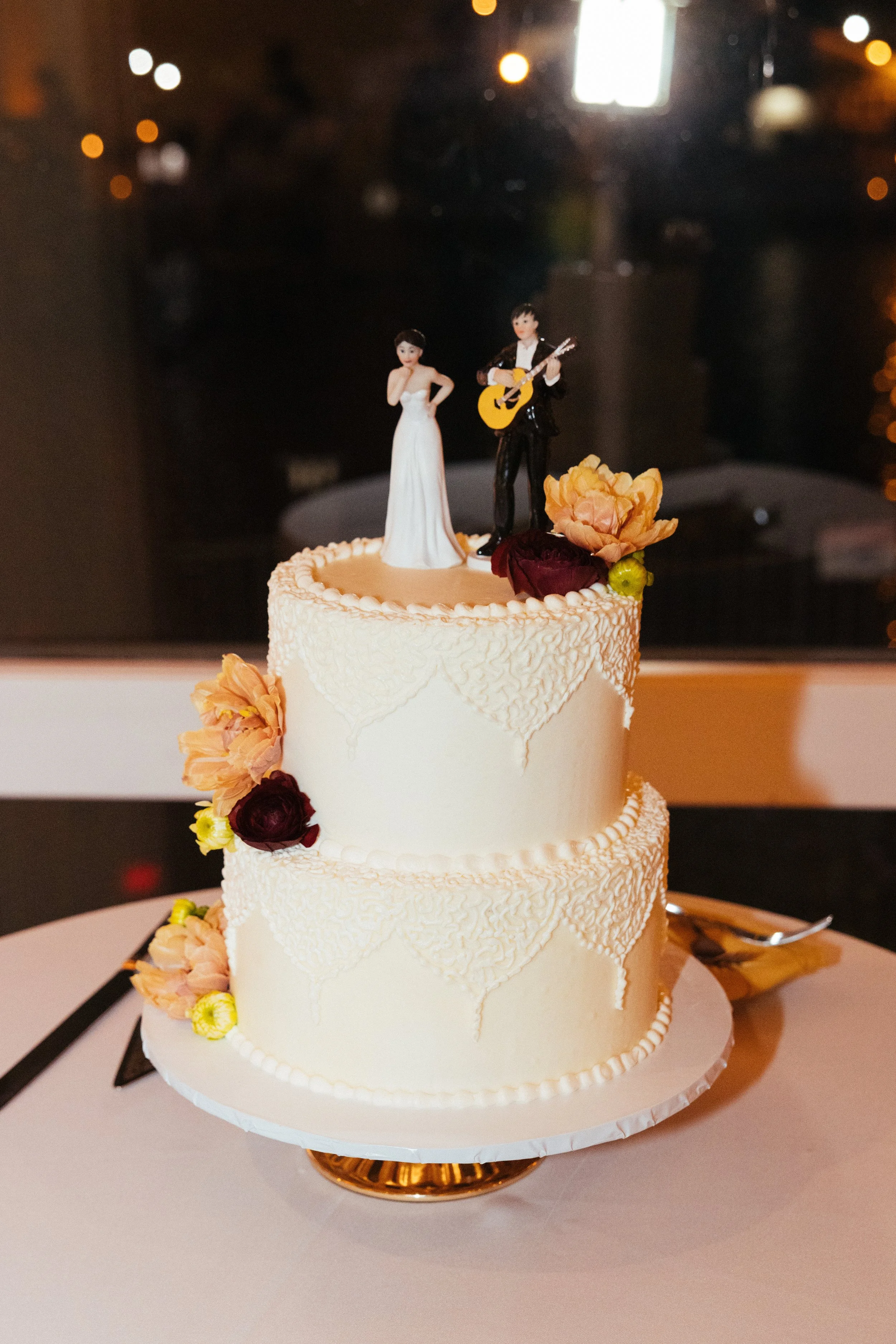 Two-tier lace wedding cake with a musician topper at a Dana Point reception