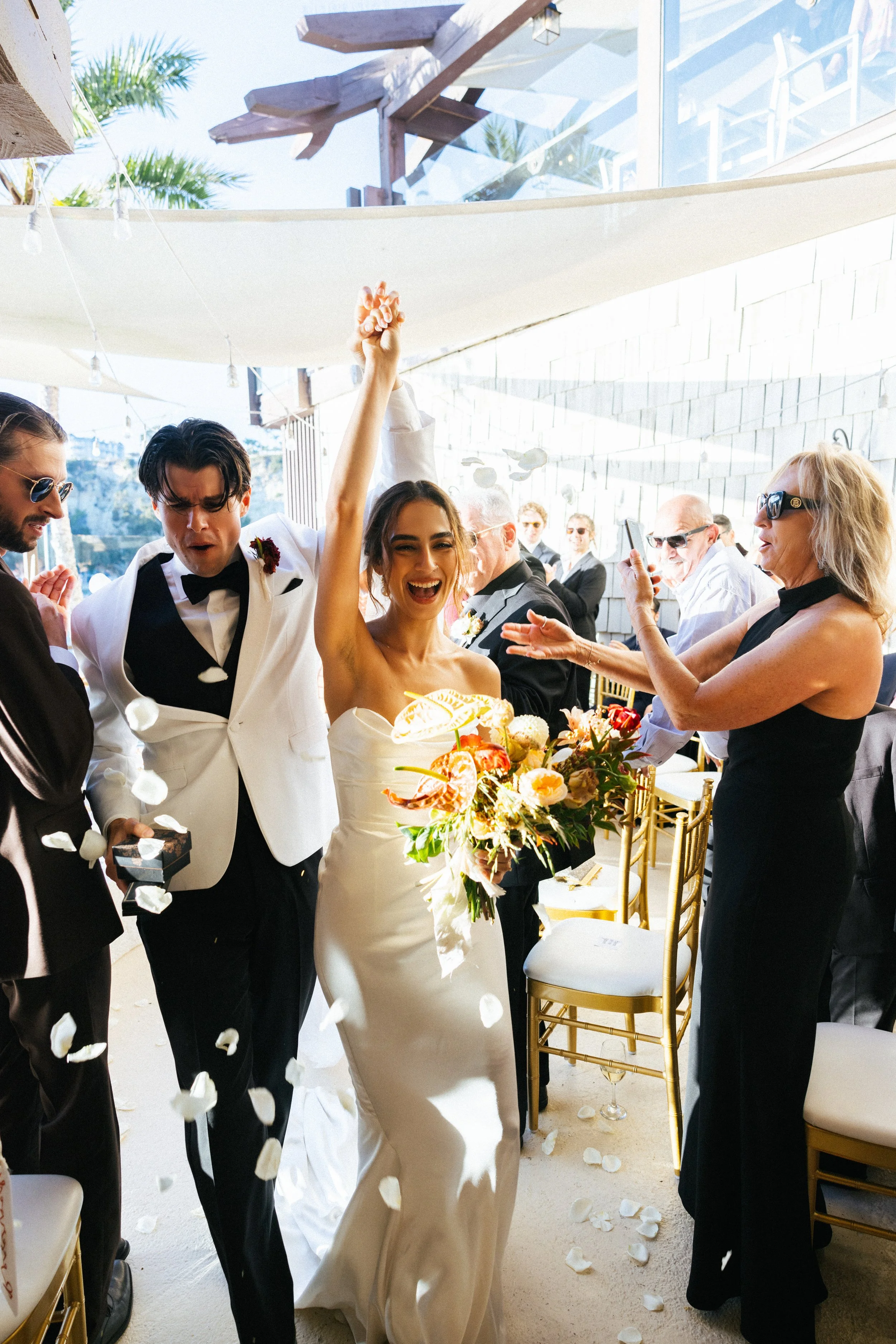Bride cheers with her bouquet during a petal-filled recessional at Dana Point Yacht Club