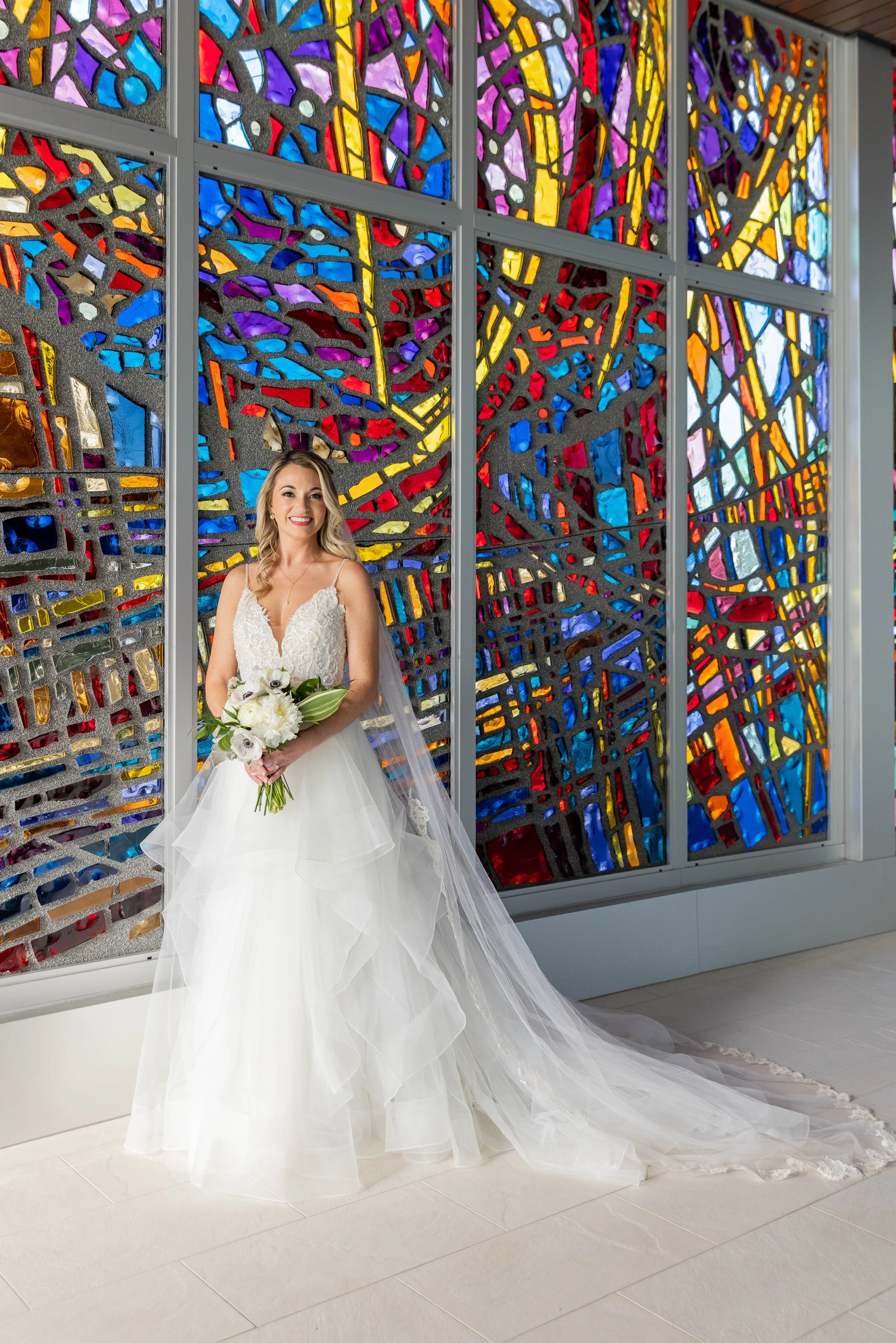 Bride with her bouquet in front of a colorful stained-glass wall on her wedding day
