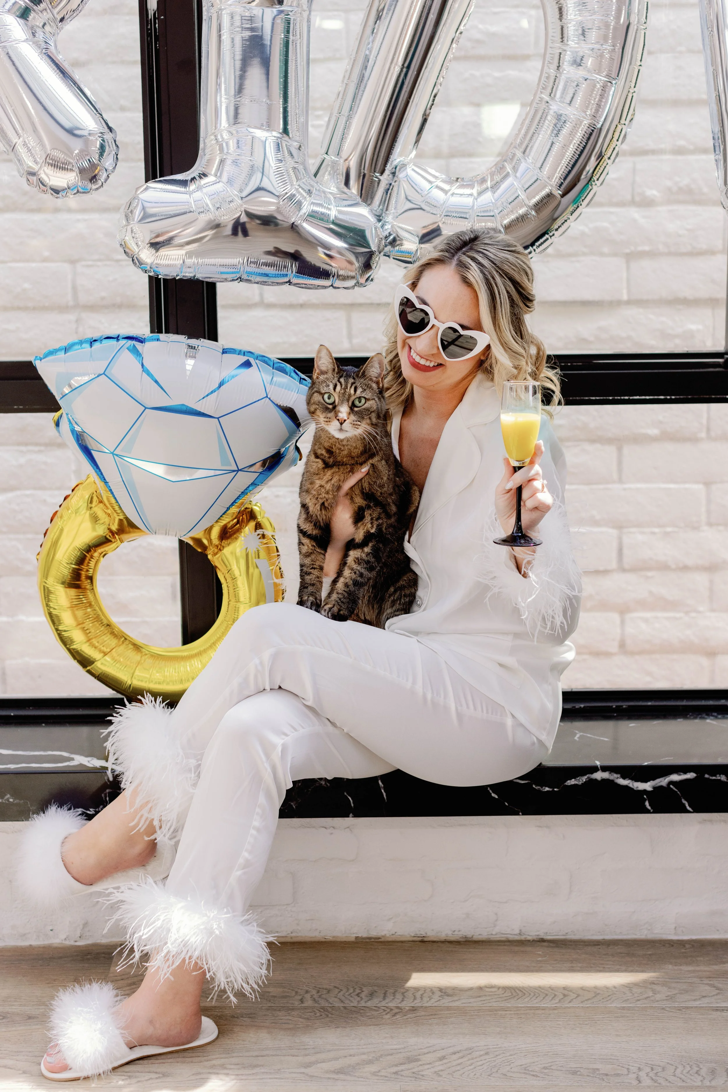 Bride in pajamas holds her cat with I Do balloons while getting ready