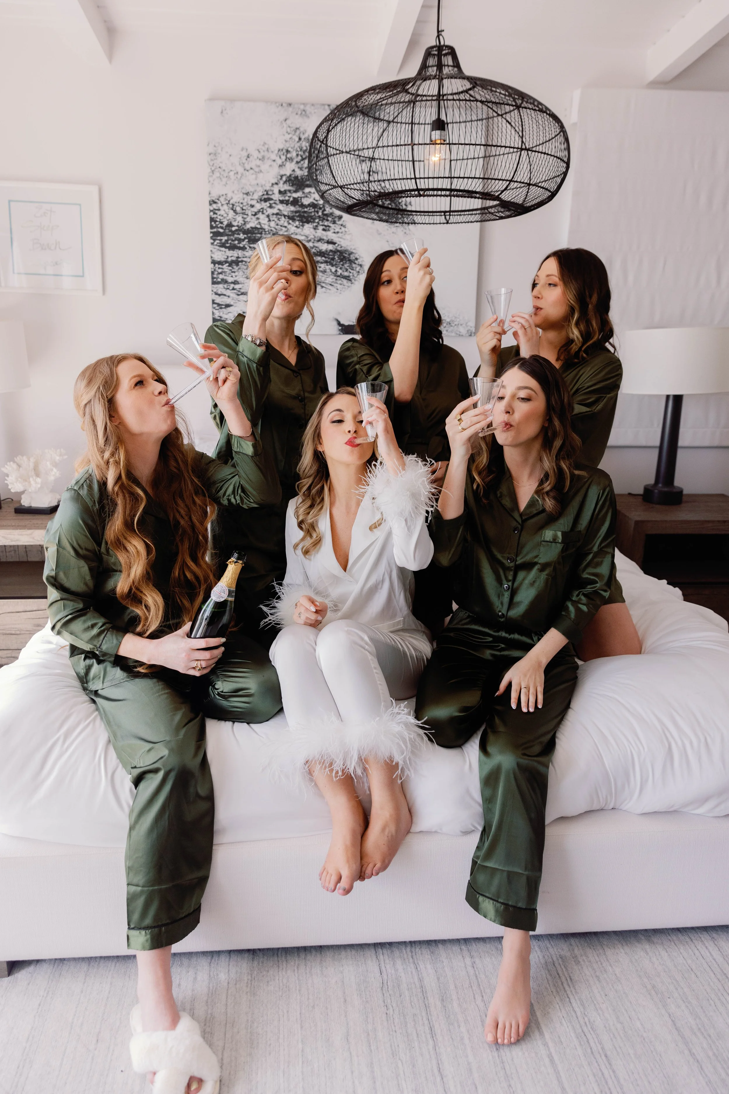 Bride and bridesmaids in matching pajamas toast champagne while getting ready