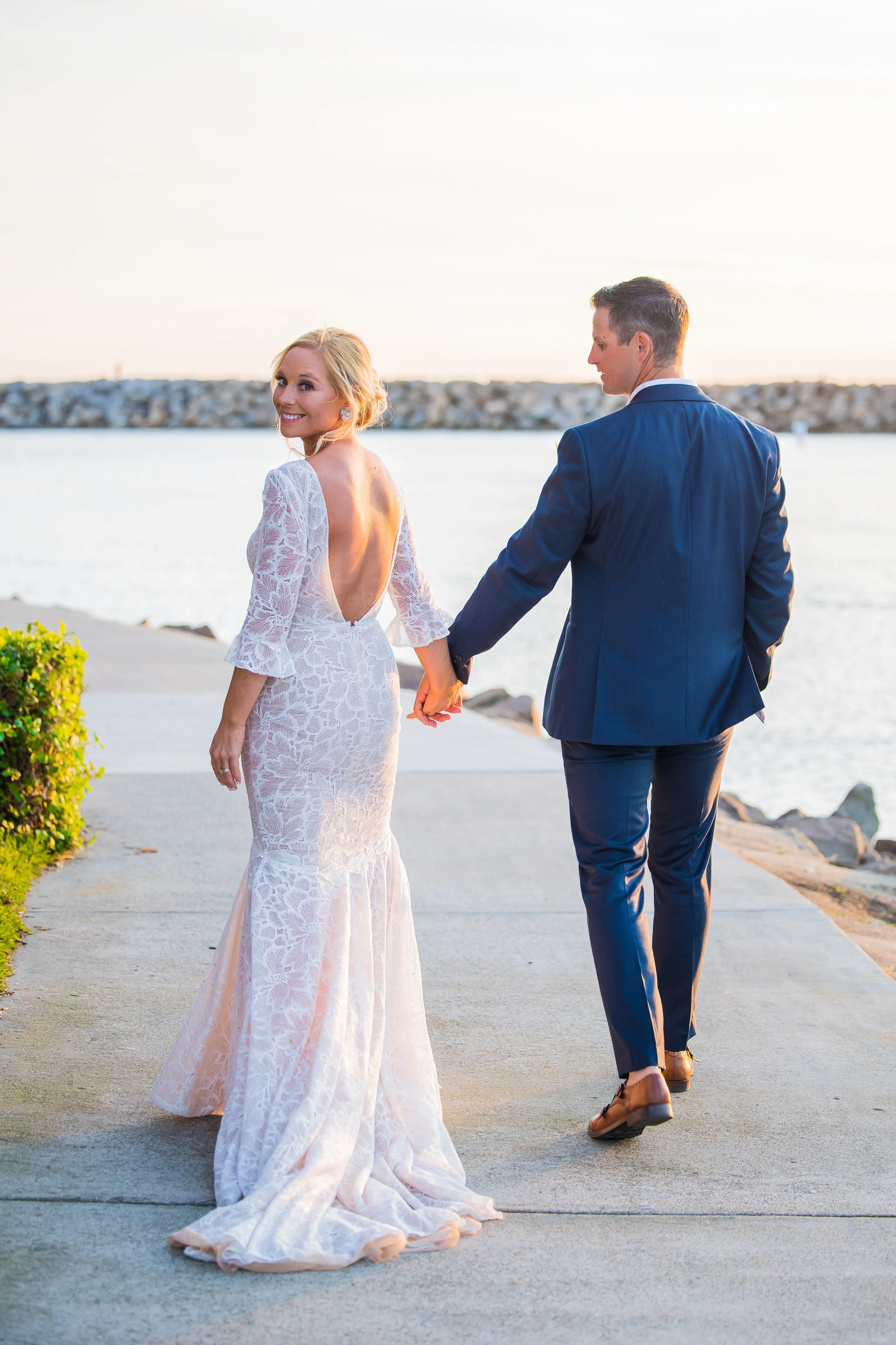 Bride looks back walking the Dana Point Harbor jetty with her groom at sunset