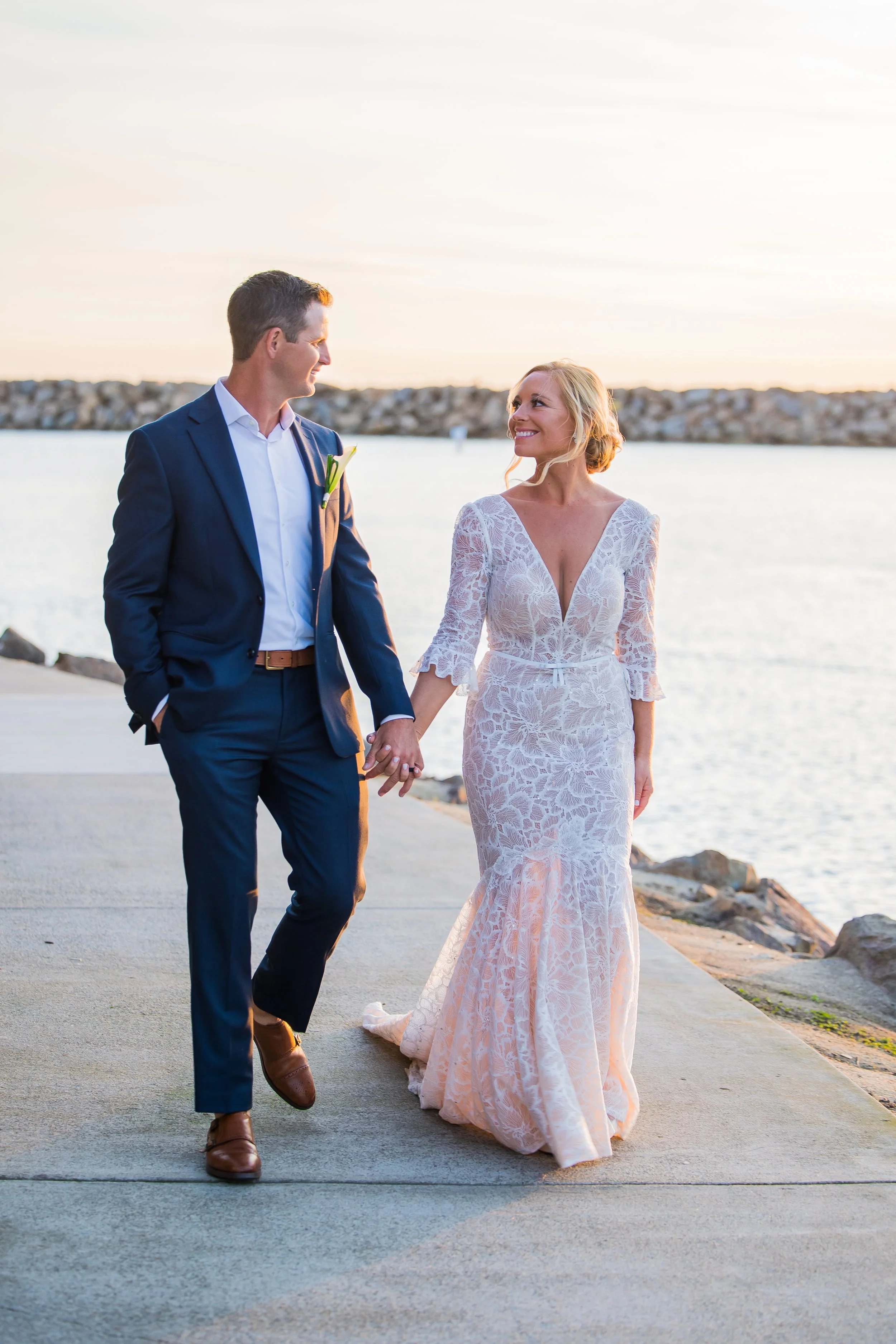 Newlyweds walk hand in hand along Dana Point Harbor at sunset