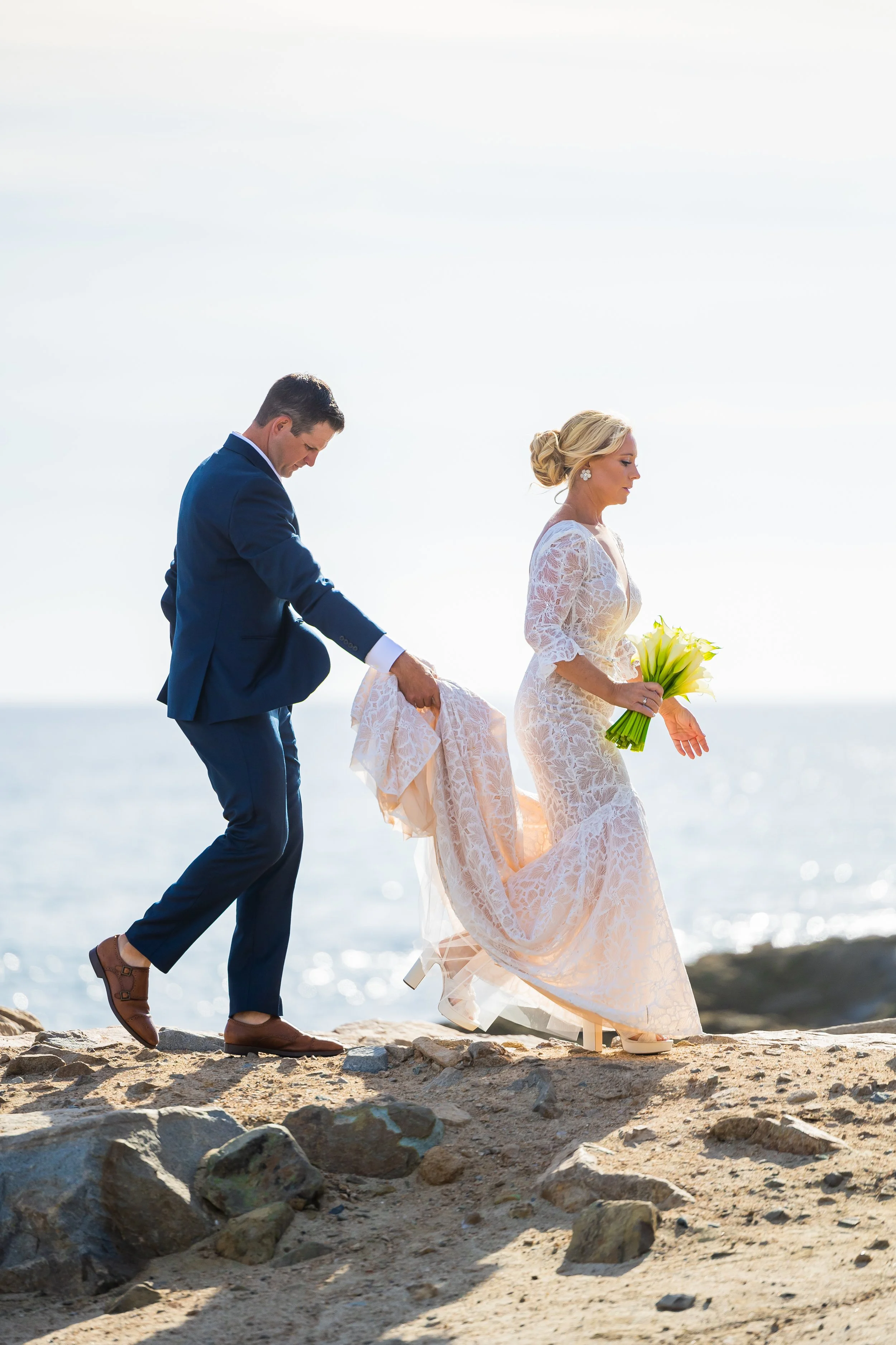 Groom helps his bride up the coastal rocks during Dana Point wedding portraits