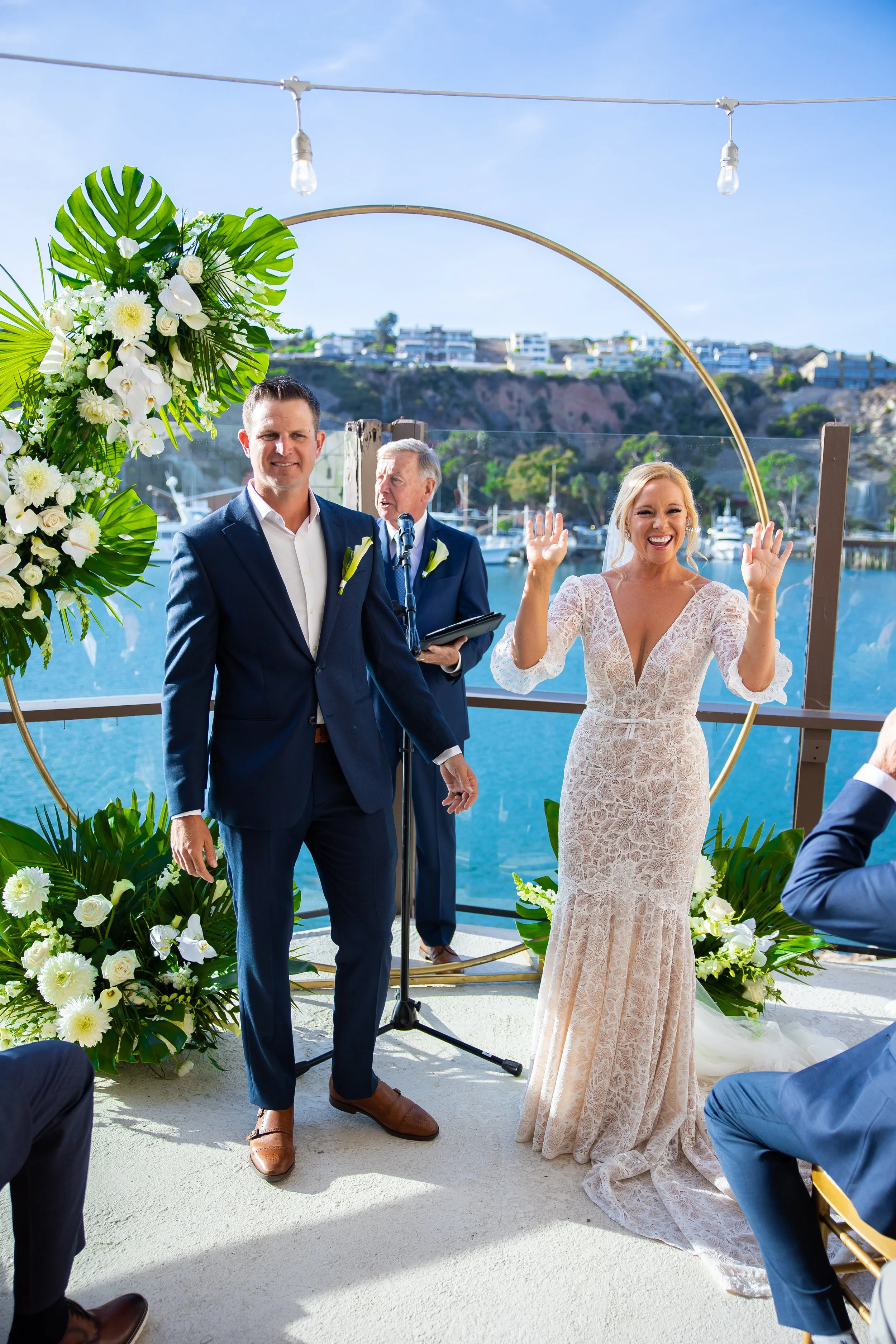 Bride celebrates at a gold circle arch over the harbor at a Dana Point Yacht Club wedding