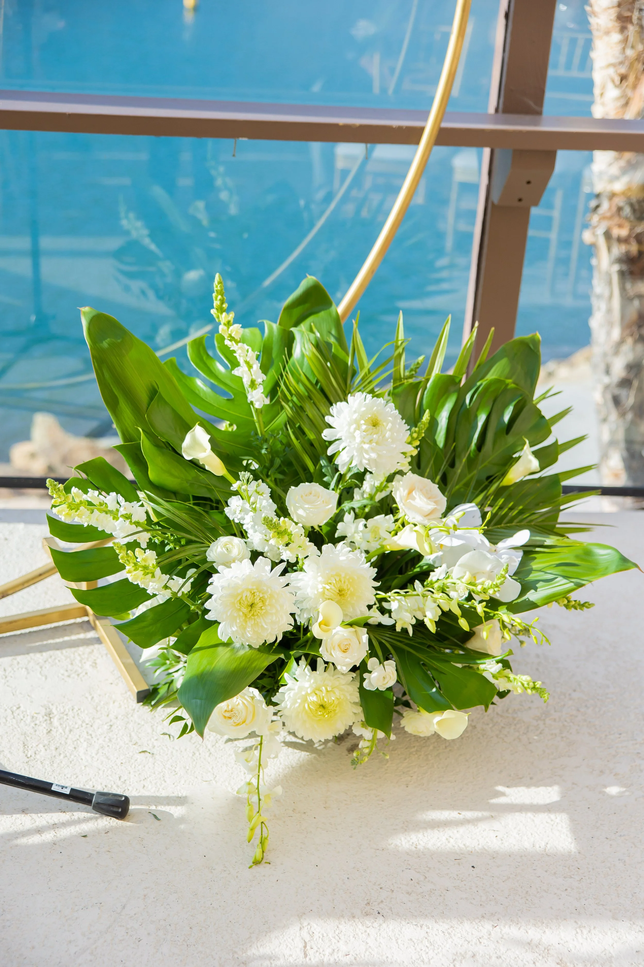 White tropical ceremony florals on a gold arch over Dana Point Harbor