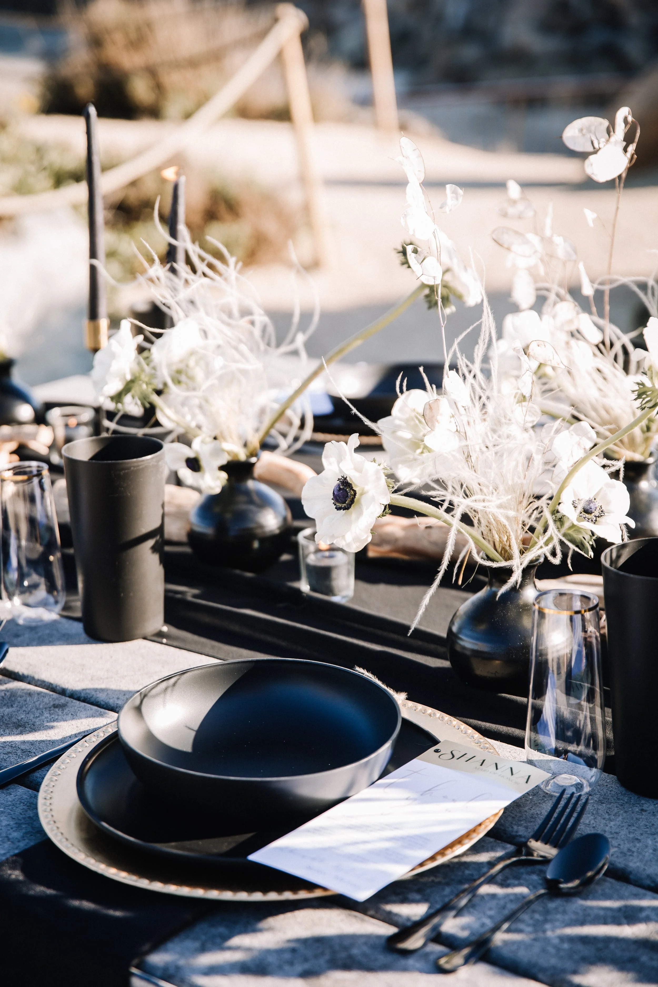 Black place setting with anemones, pampas and black taper candles at a beach wedding