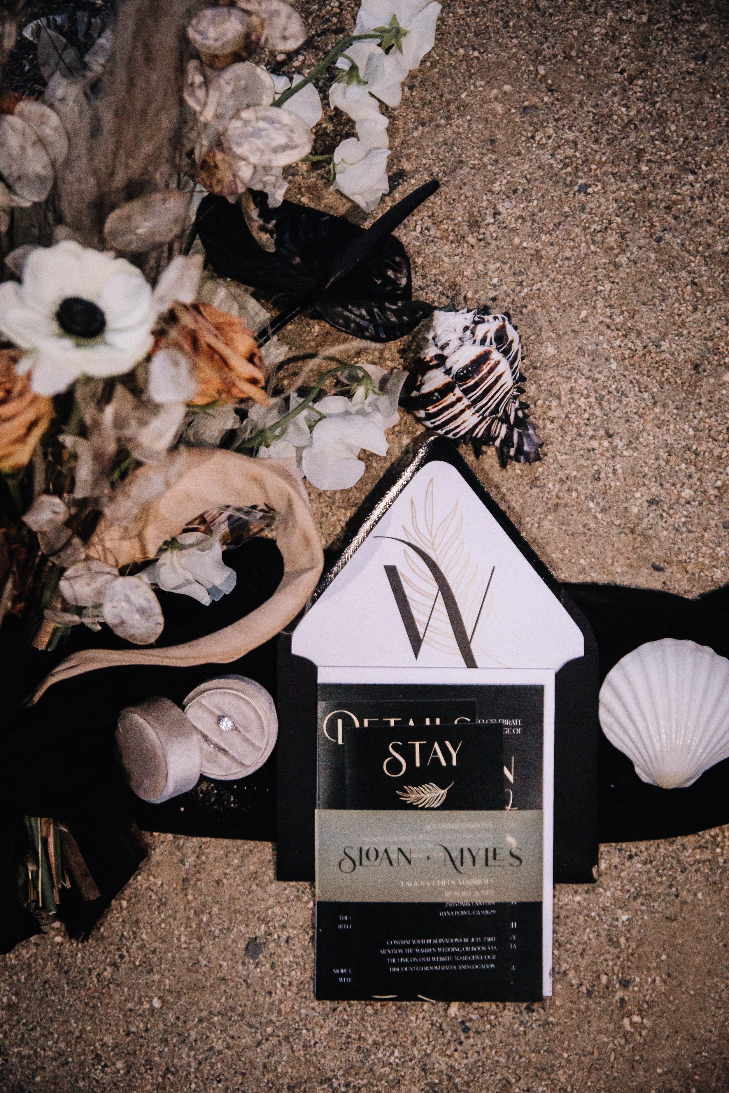 Moody black wedding invitation and ring box styled with dark florals and a seashell