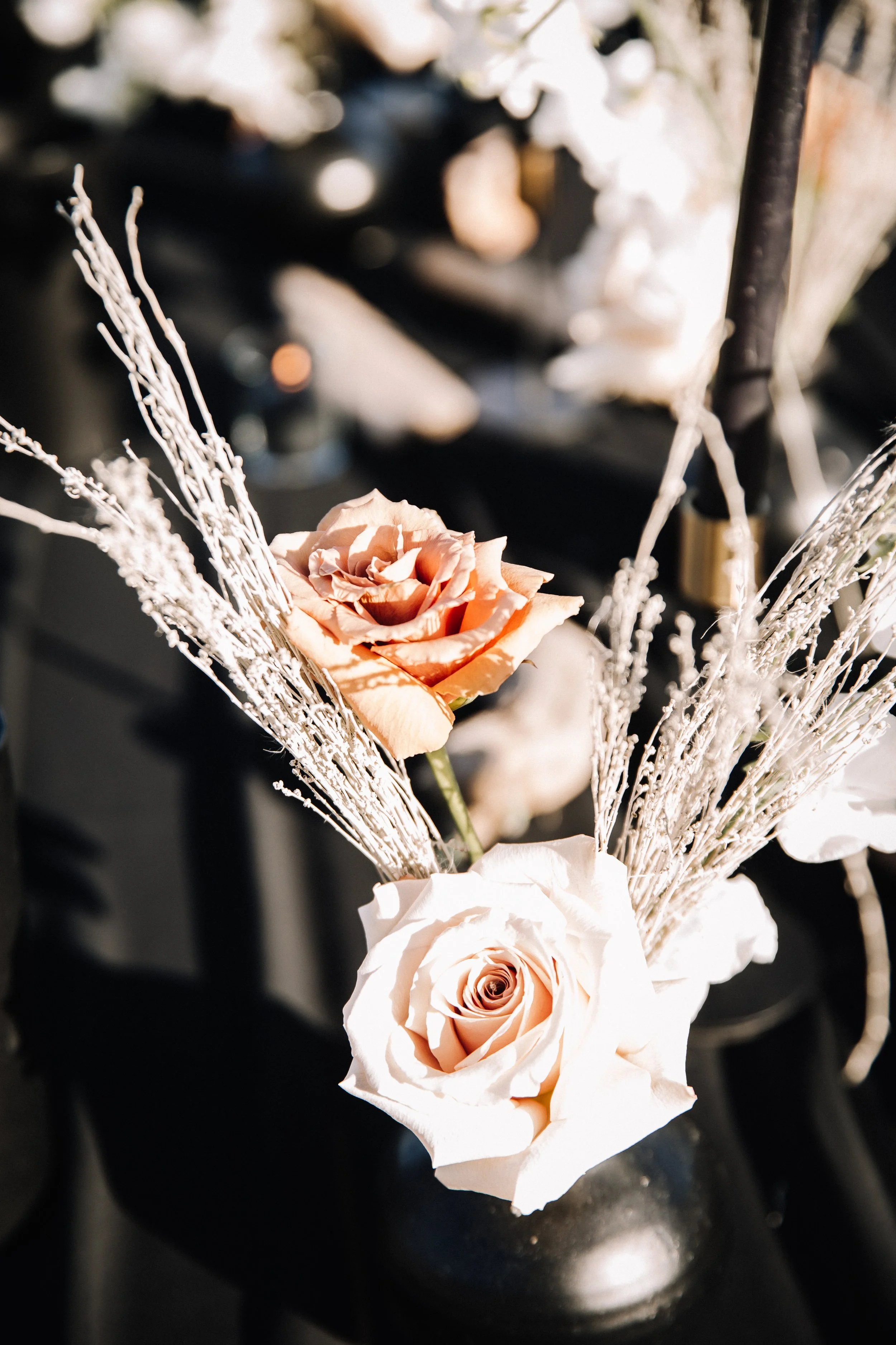 Peach and blush roses with frosted dried branches in a bud vase at a moody beach wedding