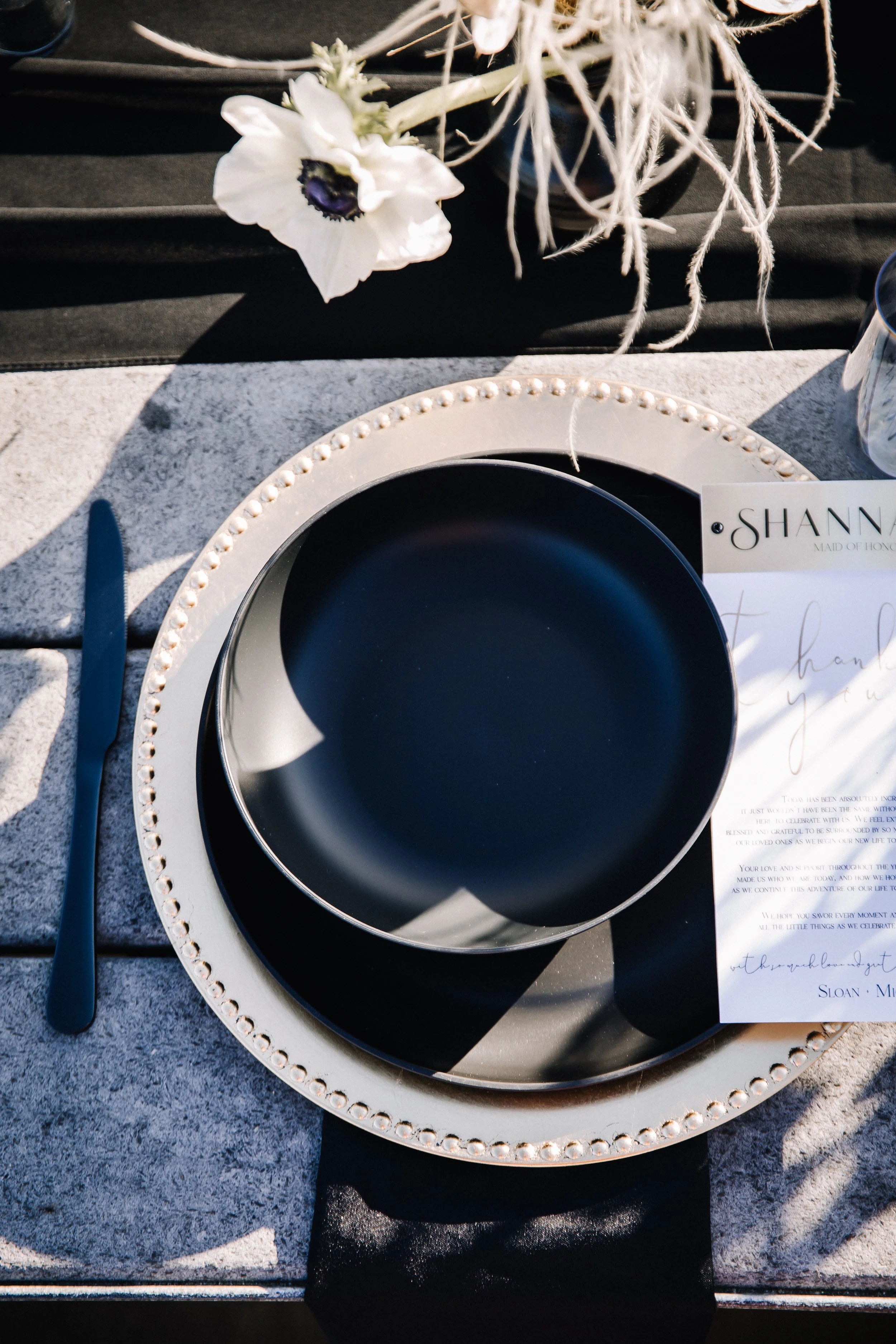 Overhead black place setting on a beaded charger with a menu card at a moody beach wedding