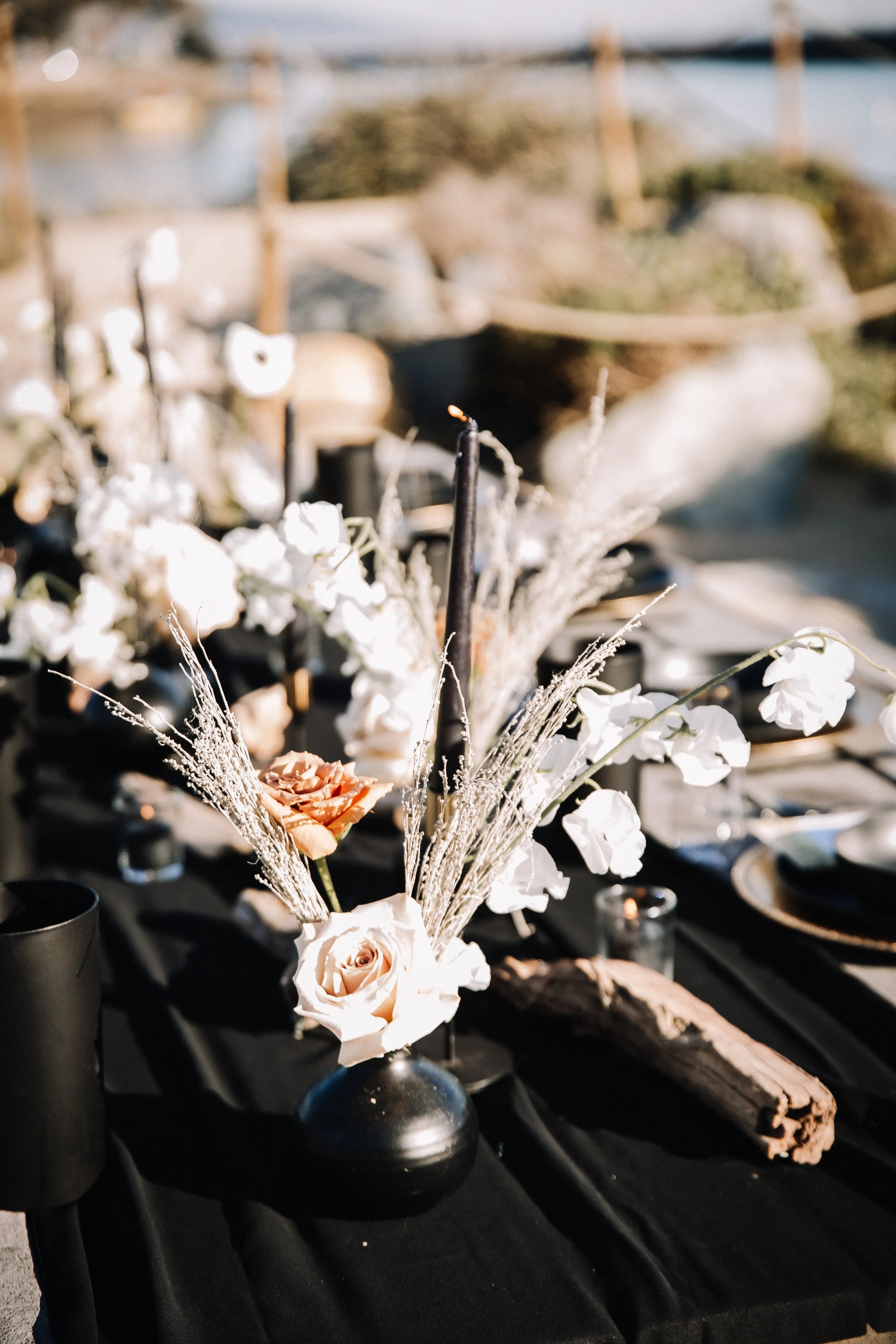 Blush roses, dried grasses and a black taper candle with driftwood at a Dana Point beach wedding