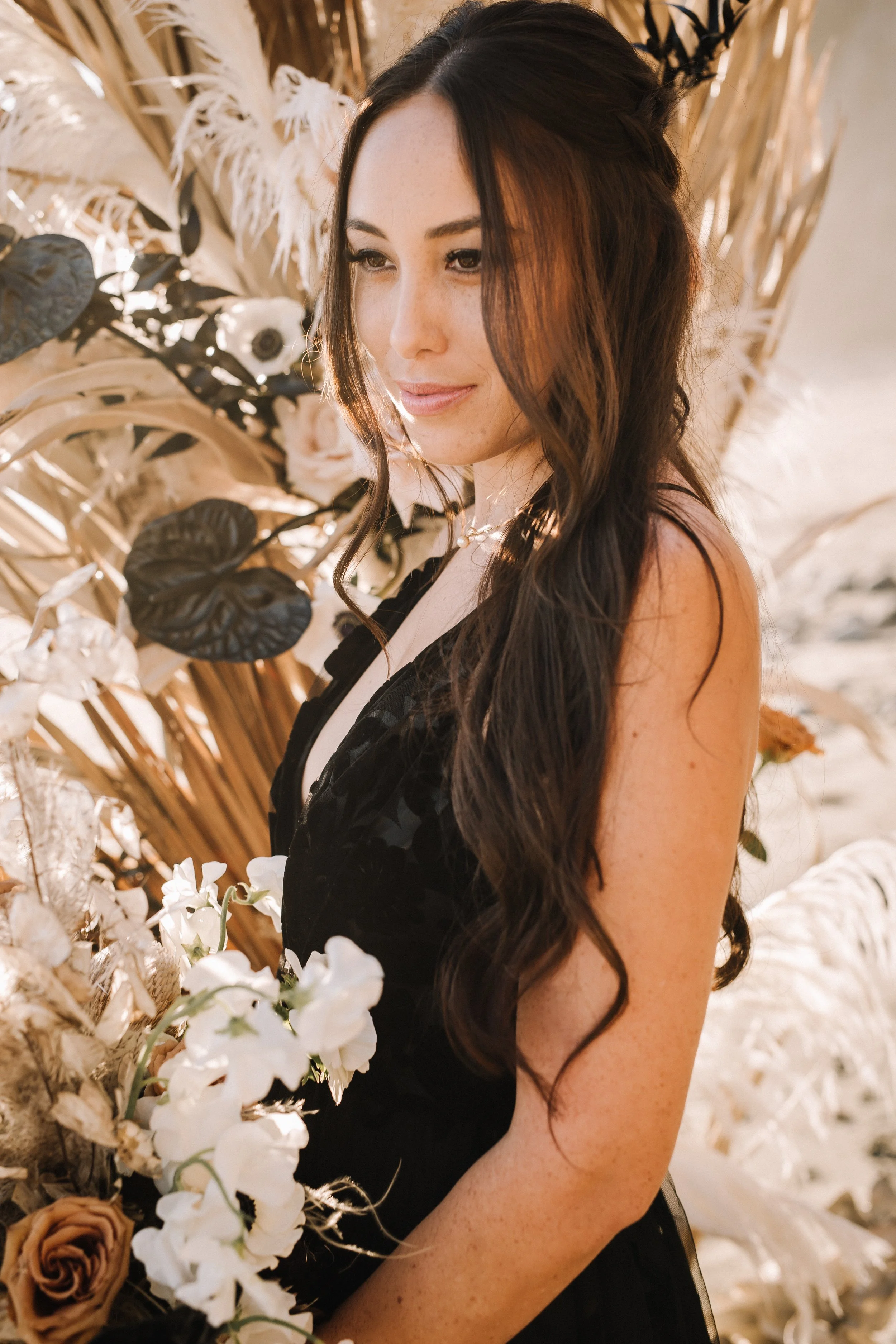 Portrait of a bride in a black floral-lace gown holding white sweet peas at an alternative beach wedding