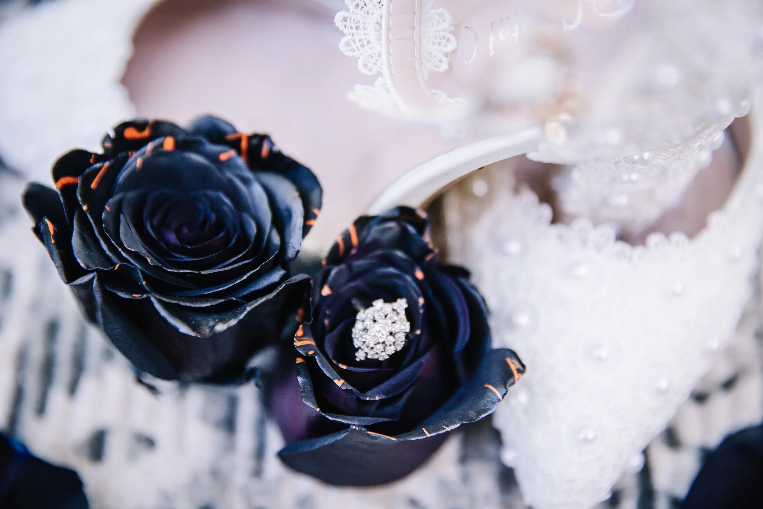 Moody wedding detail flat lay featuring black roses, white florals, wedding rings, lace, and dramatic Halloween-inspired styling.