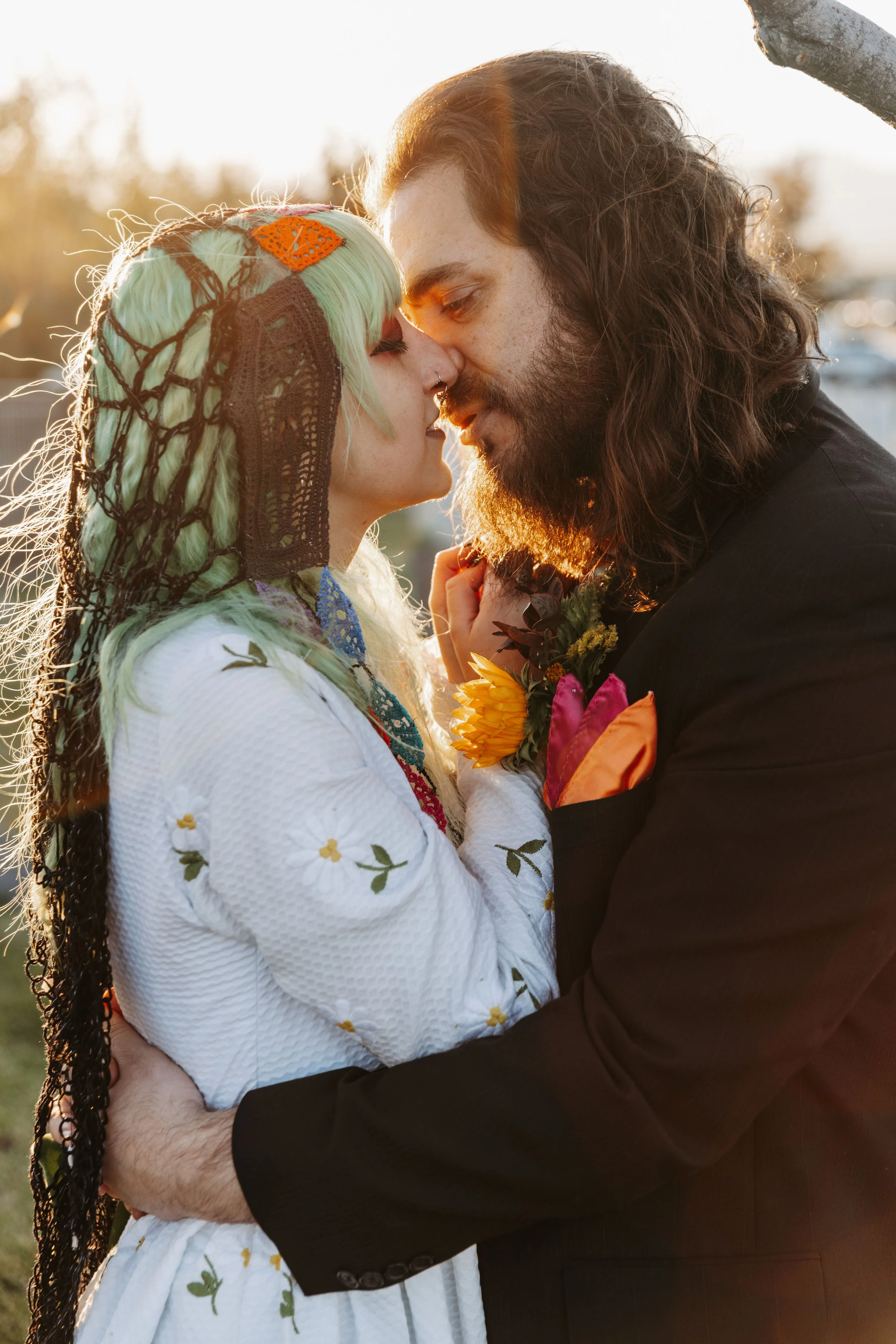 Close-up golden hour portrait of a couple embracing during their Día de los Muertos-inspired wedding, highlighting colorful handmade details and vibrant floral accents.