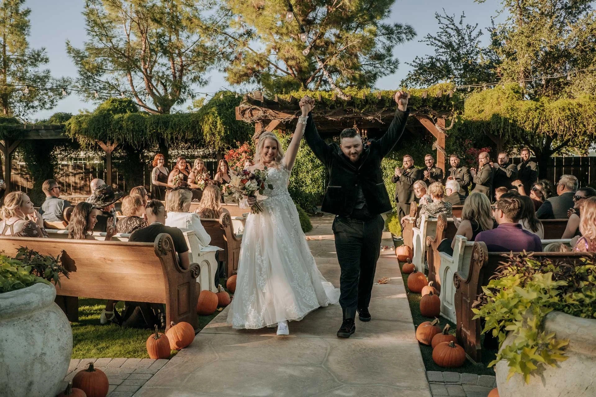 alternative wedding couple walking down the aisle with their hands in the air 