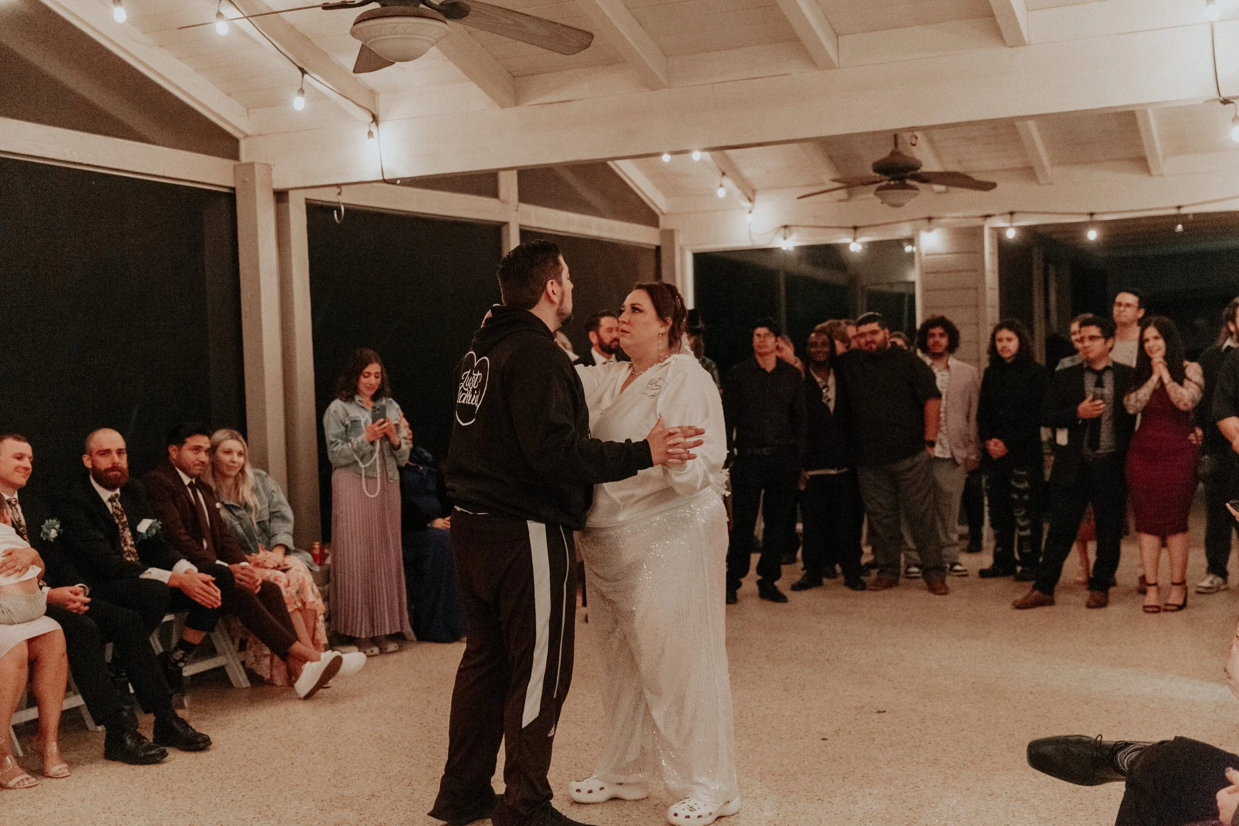 Newlywed couple sharing casual first dance in matching hoodies and Crocs surrounded by wedding guests