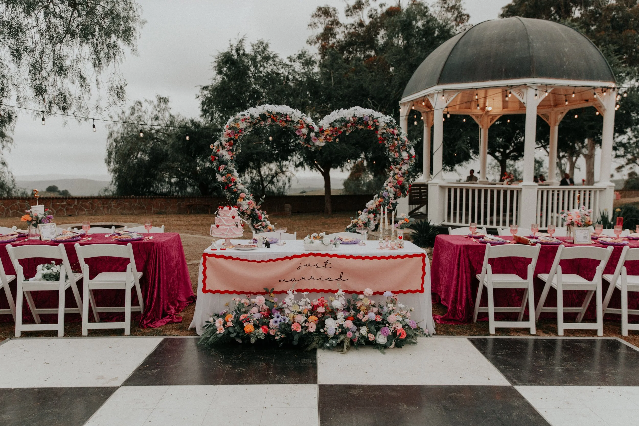 Bold colorful wedding reception design with heart-shaped floral arch, vibrant tablescapes, and romantic outdoor gazebo setup
