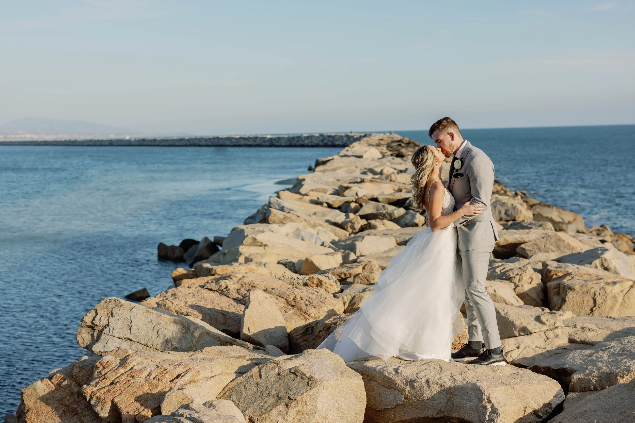 Bride and groom kiss on the Dana Point Harbor breakwater, a scenic spot near the top Dana Point wedding venues