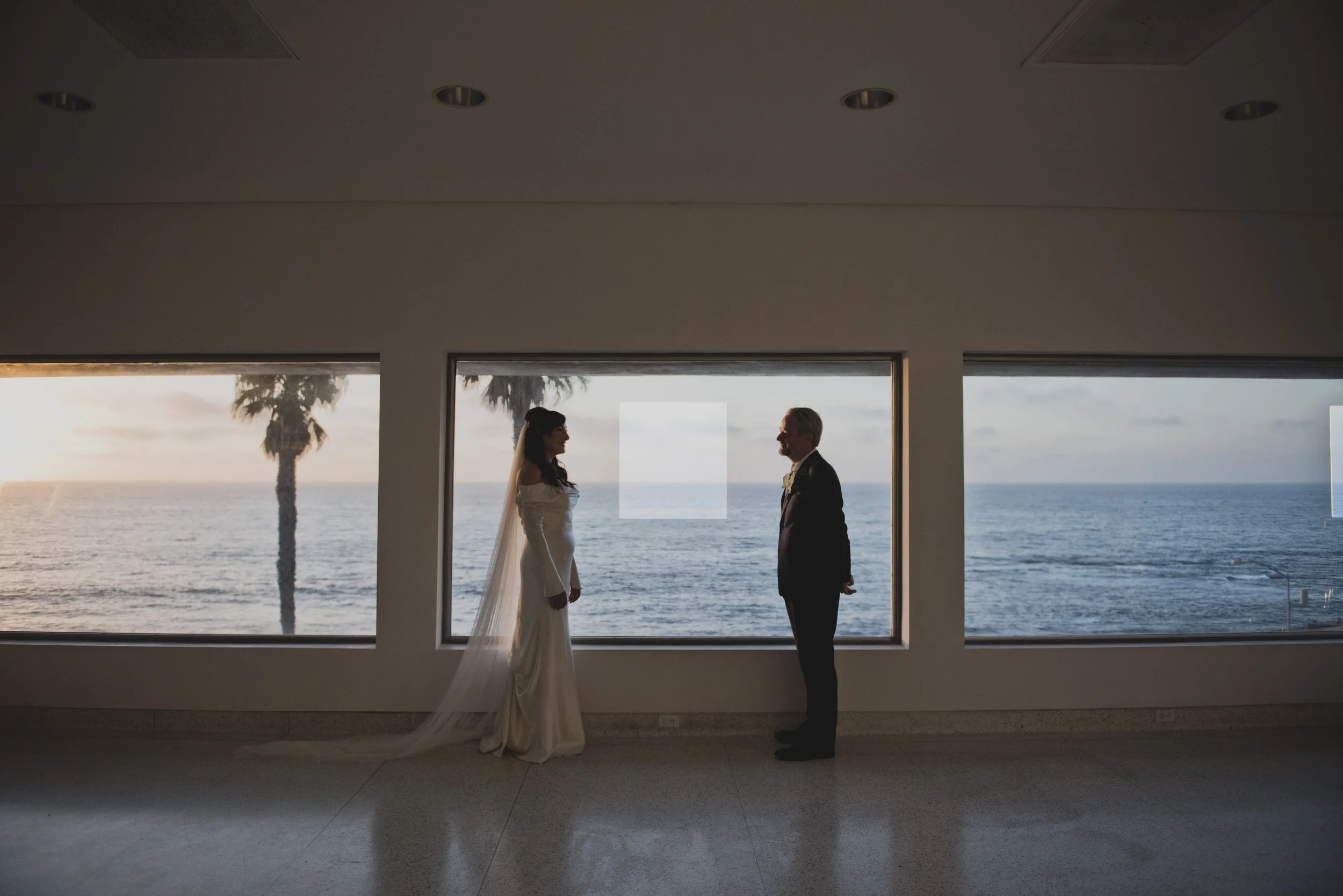 Bride and groom standing apart in a spacious contemporary art gallery with scenic ocean view
