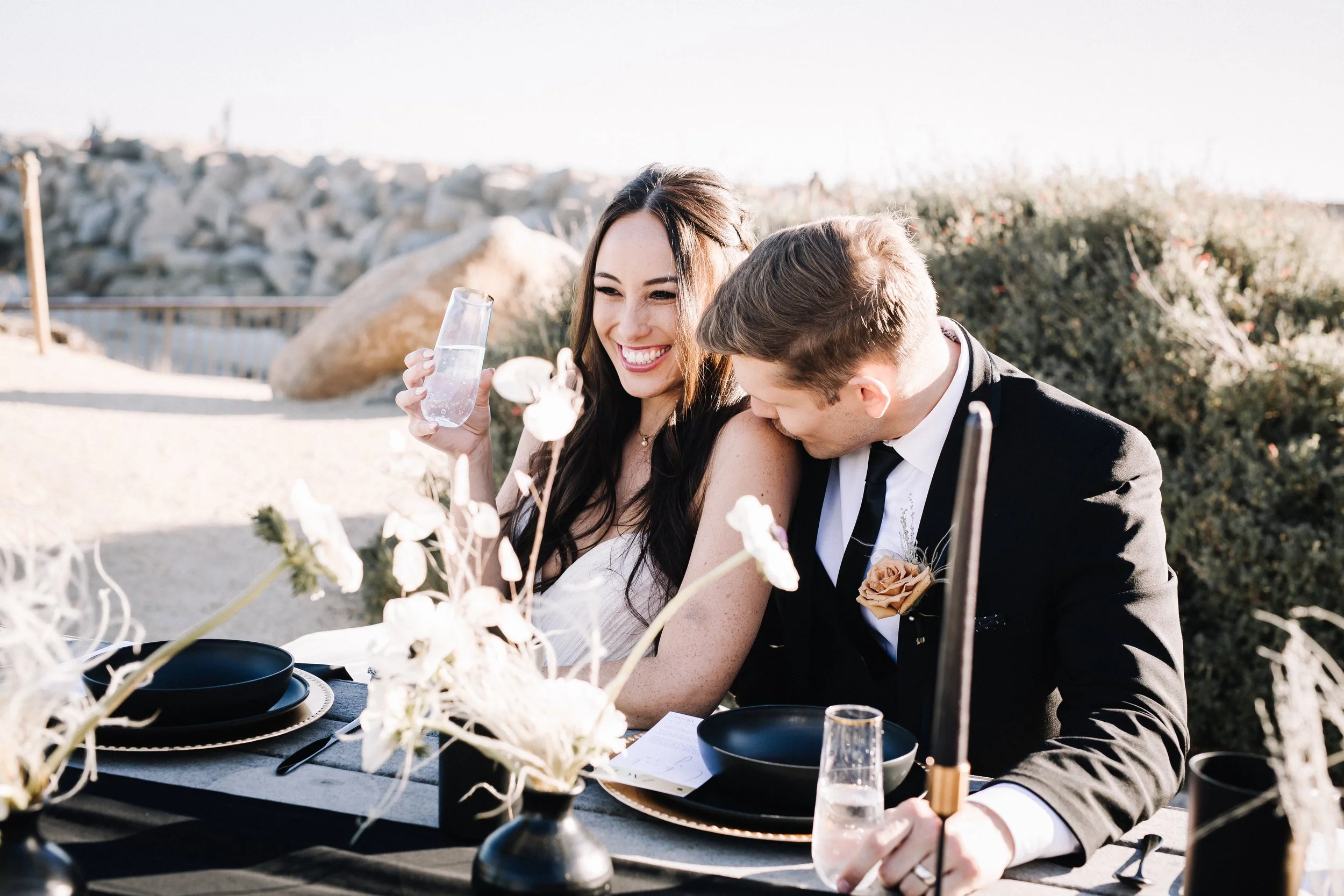 Couple toasting at a moody beach wedding reception table in Dana Point