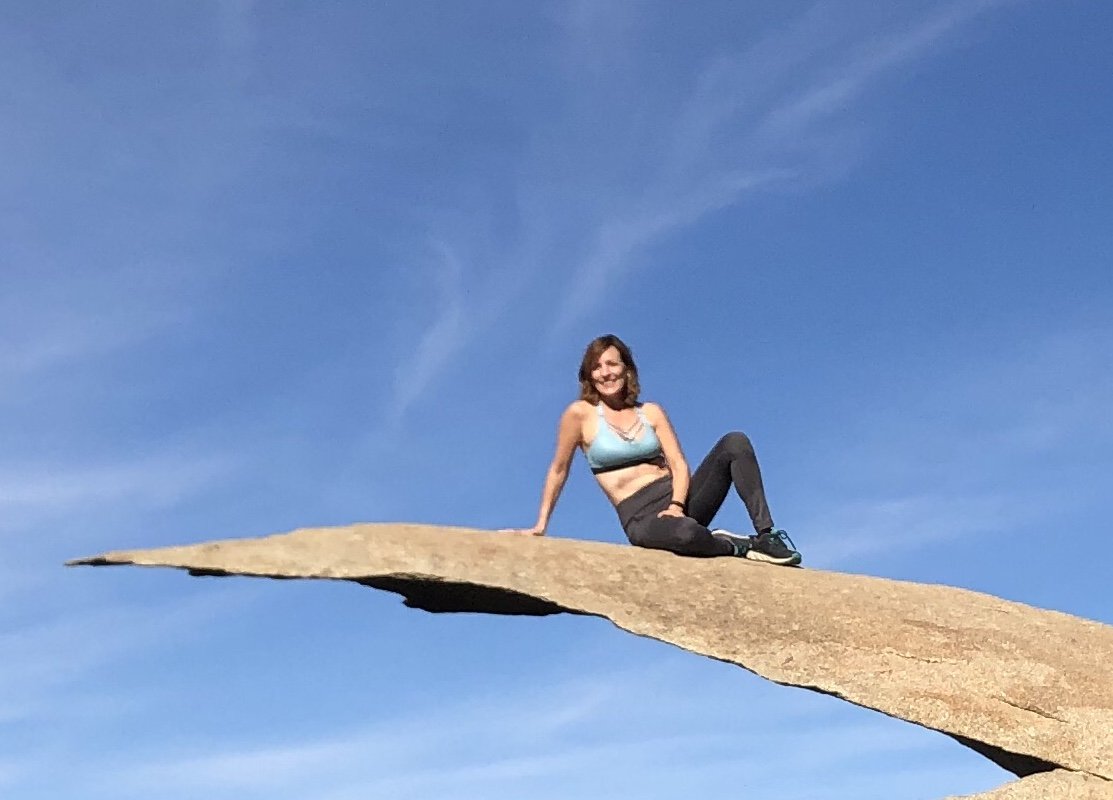 Lisa Espinoza sitting on high rock jutting out above ground called Potato Chip rock in San Diego.