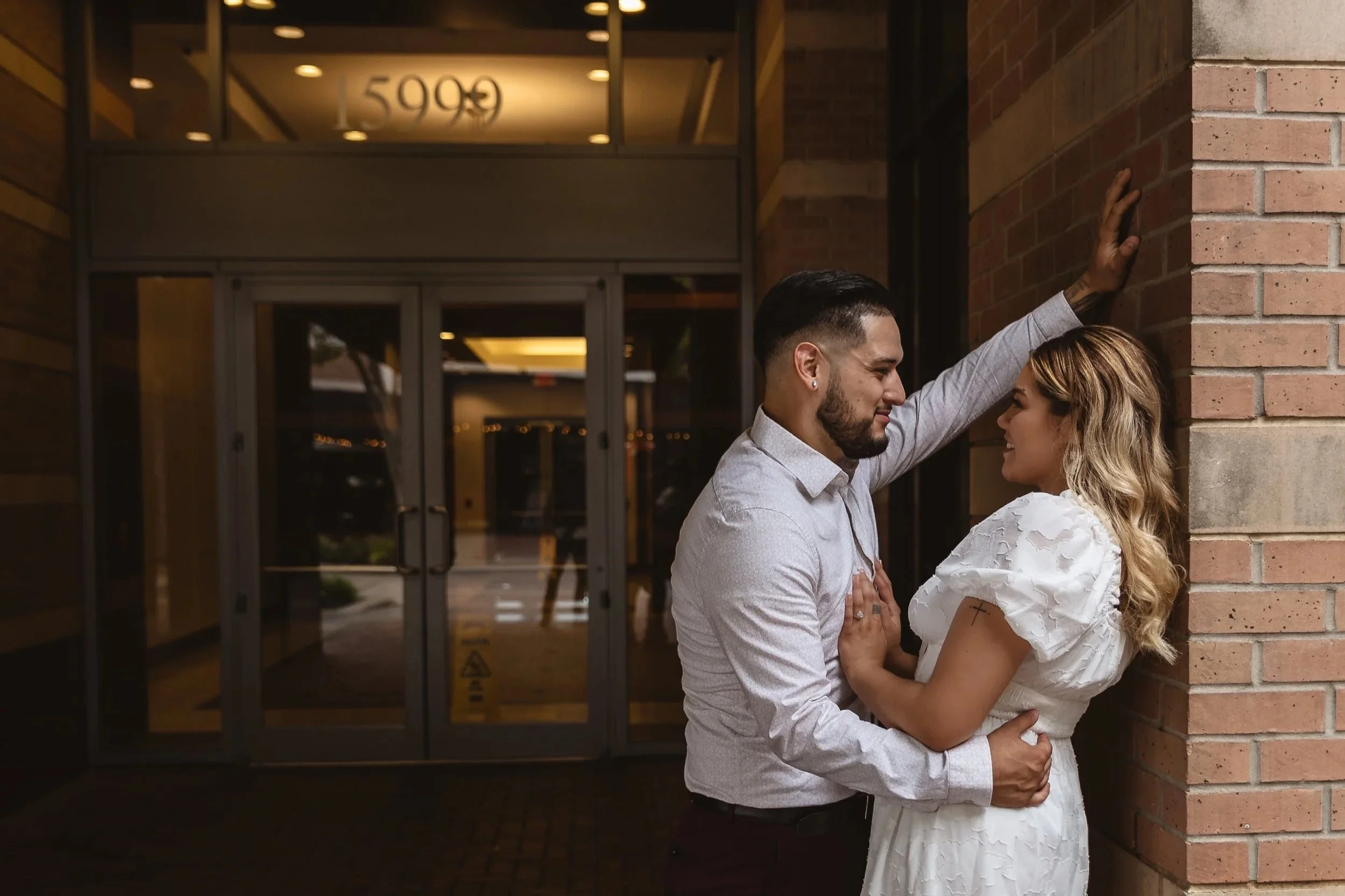 A couple in formal attire embracing outside a building with the street number 5999 above the entrance.