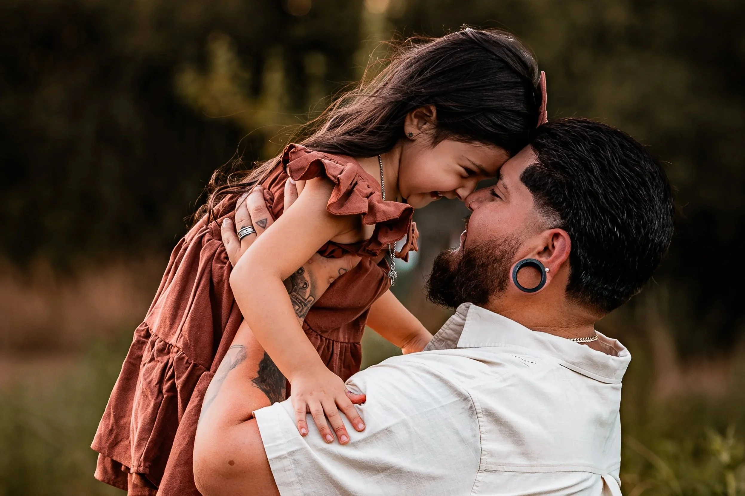 A man holding a young girl in his arms outdoors, touching their foreheads together and smiling.