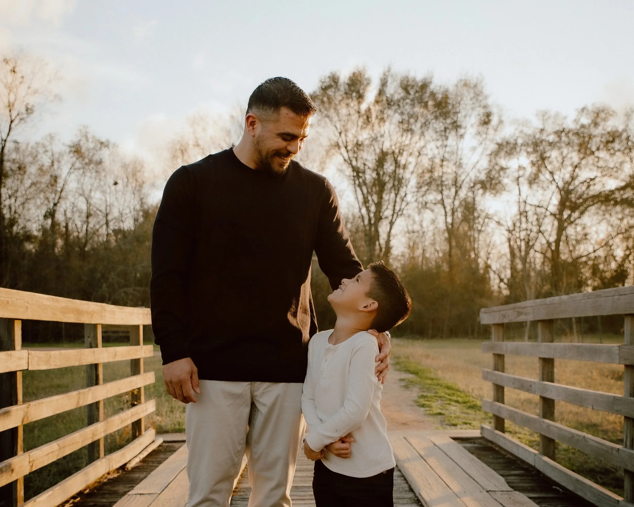 A man and a boy sharing a happy moment on a wooden bridge during sunset.