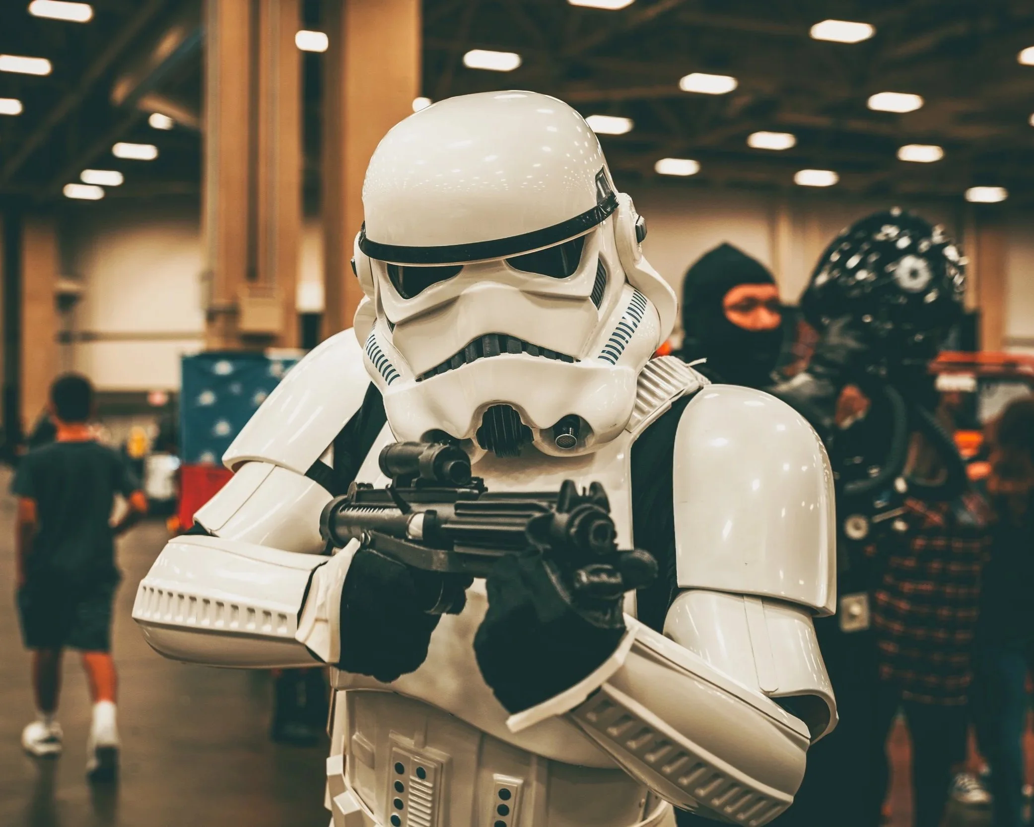 A person dressed in a Stormtrooper costume from Star Wars holding a blaster at an indoor event.