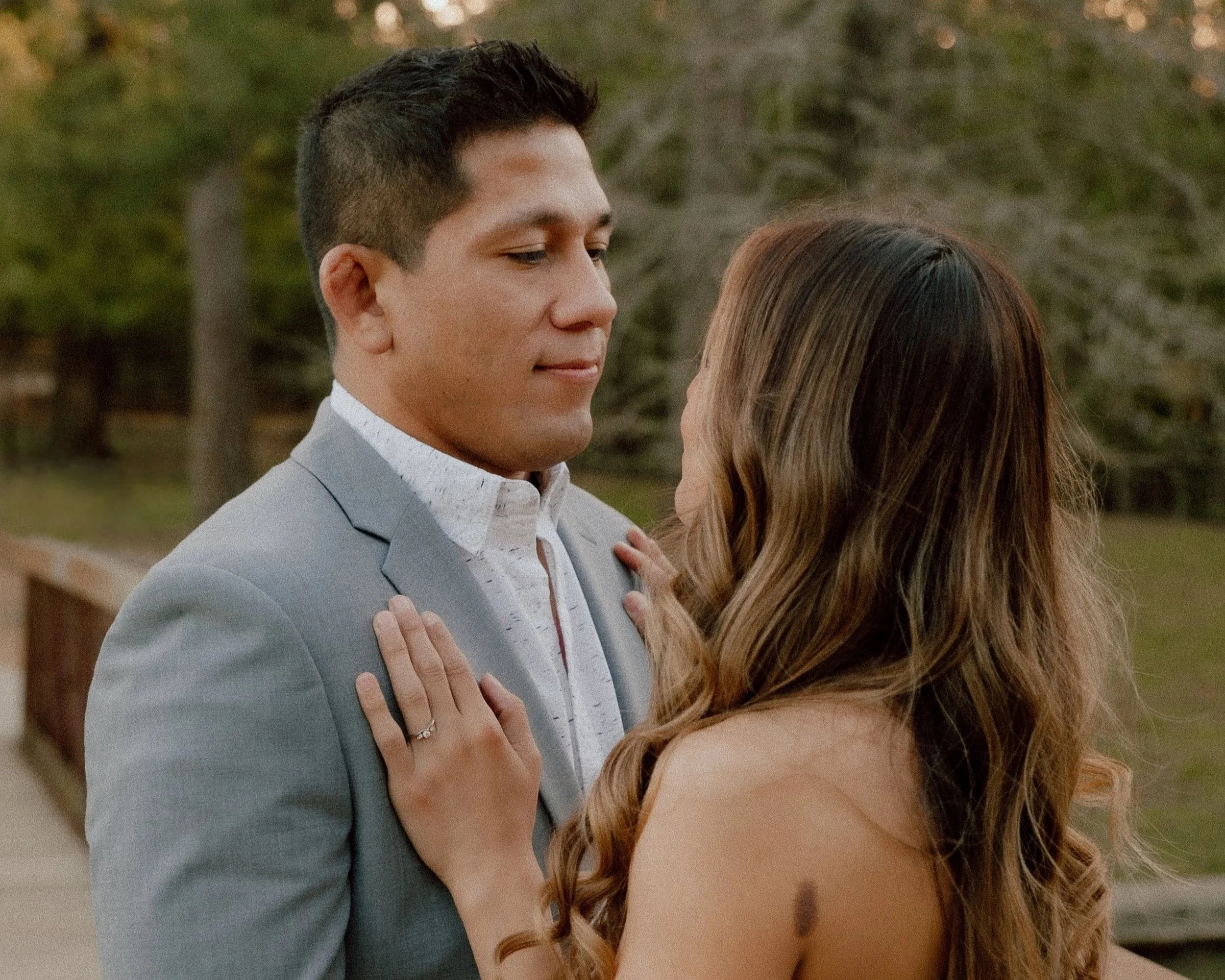 A man and woman dancing outside, looking at each other lovingly with trees in the background.
