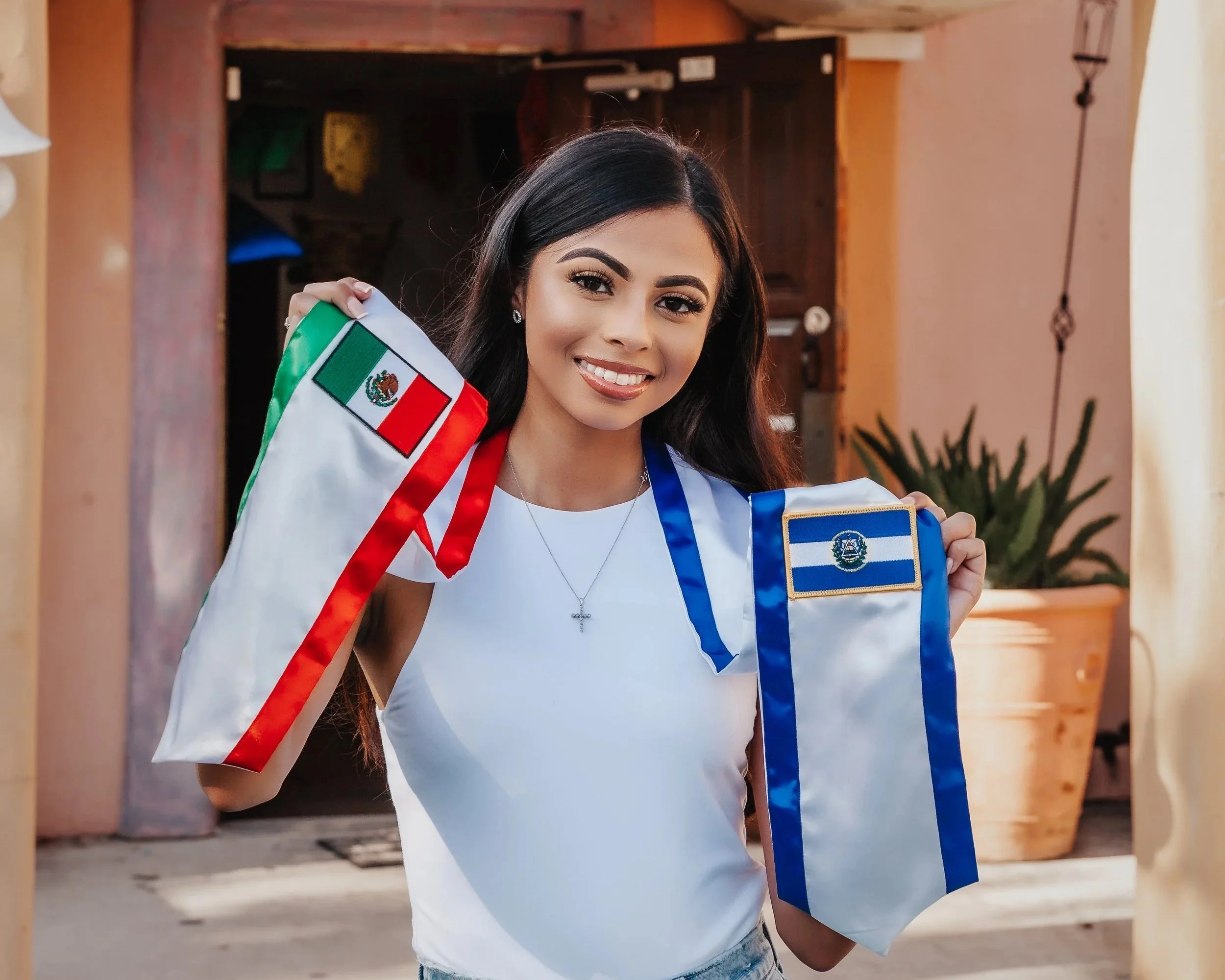 A young woman smiling and holding flags of Mexico and El Salvador.