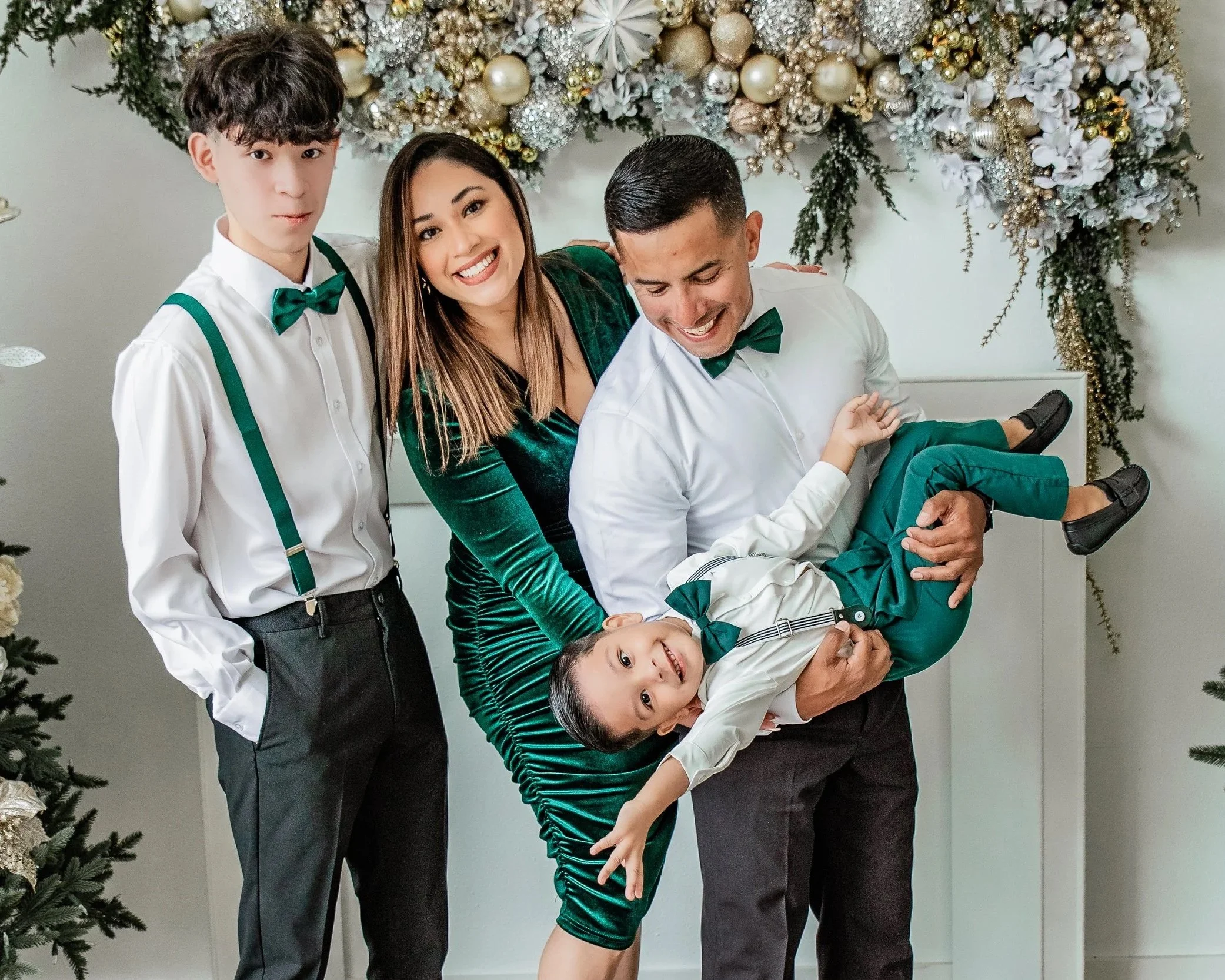 A family celebrating Christmas, with a decorated tree and festive decor in the background. The family includes three adults and one child, all dressed in festive attire, smiling and enjoying the moment.