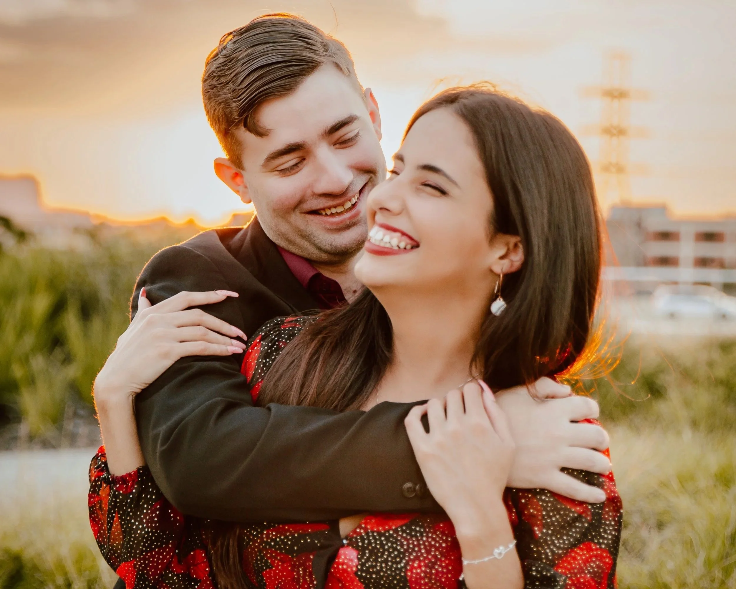 A happy couple sharing an embrace at sunset outdoors, smiling and laughing.
